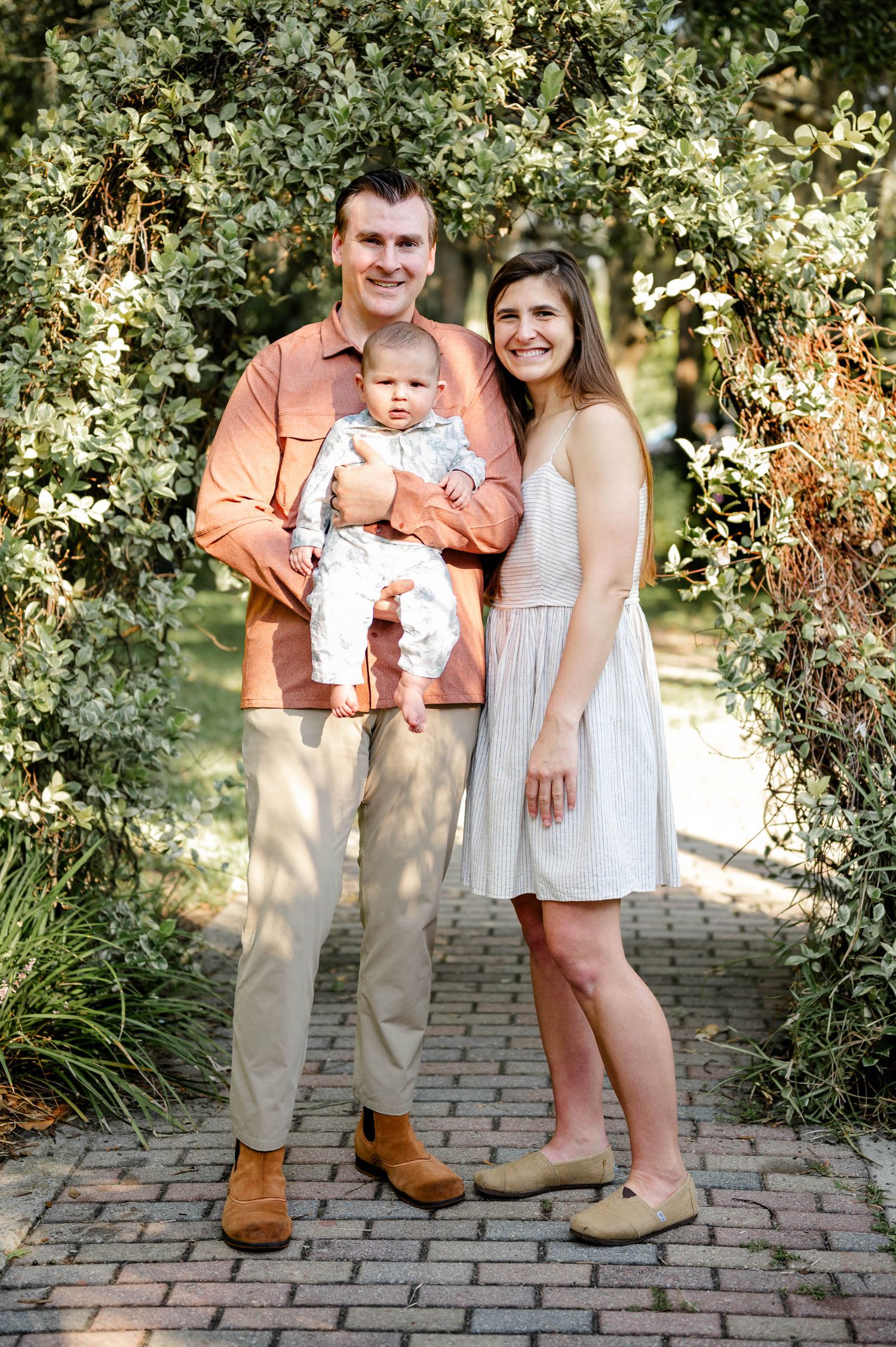 Family in coordinating coral and white outfits pose on a stone path surrounded by greenery at a spring mini session in jacksonville, fl