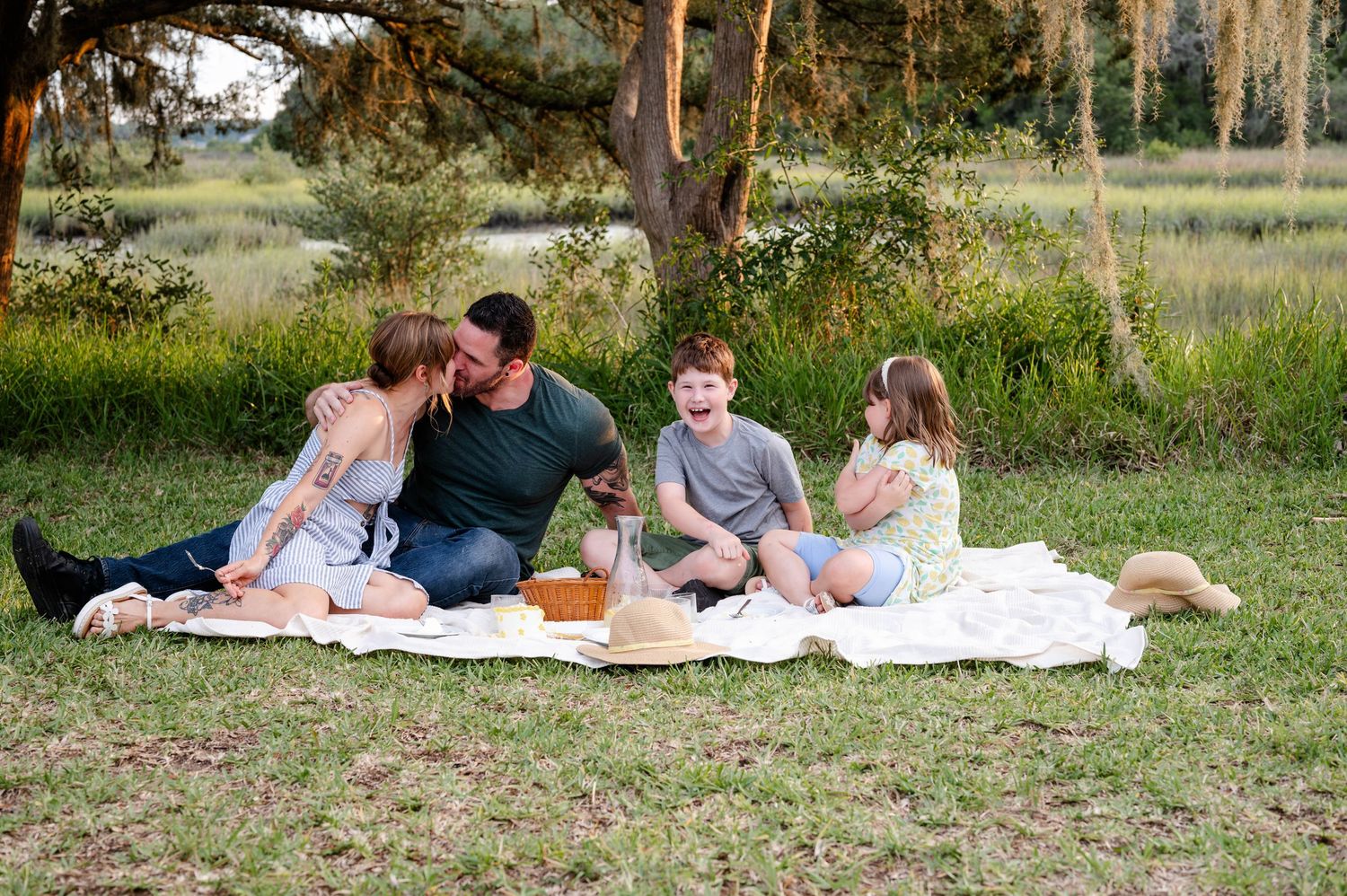 Family lying on white blanket for outdoor photoshoot in grassy field.