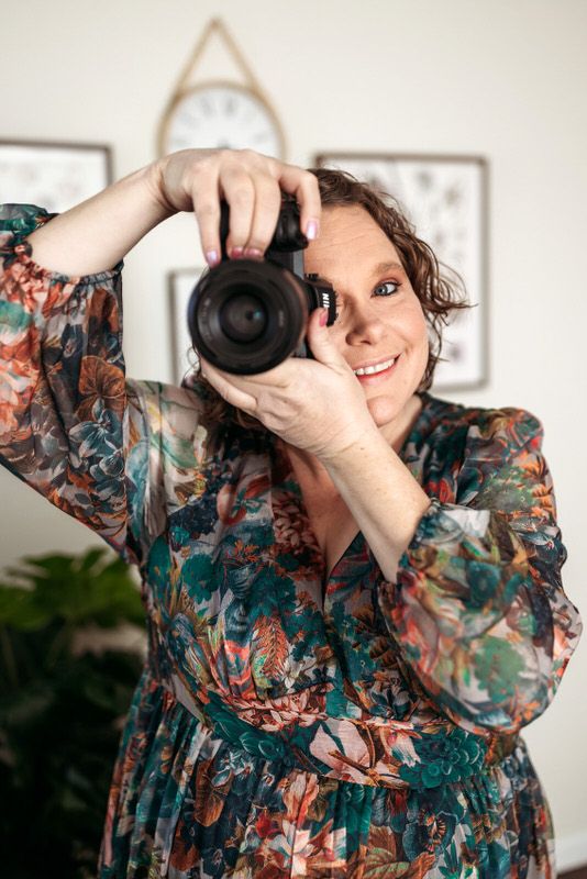 Jessica holding camera wearing floral print dress during a Jacksonville indoor photography session.