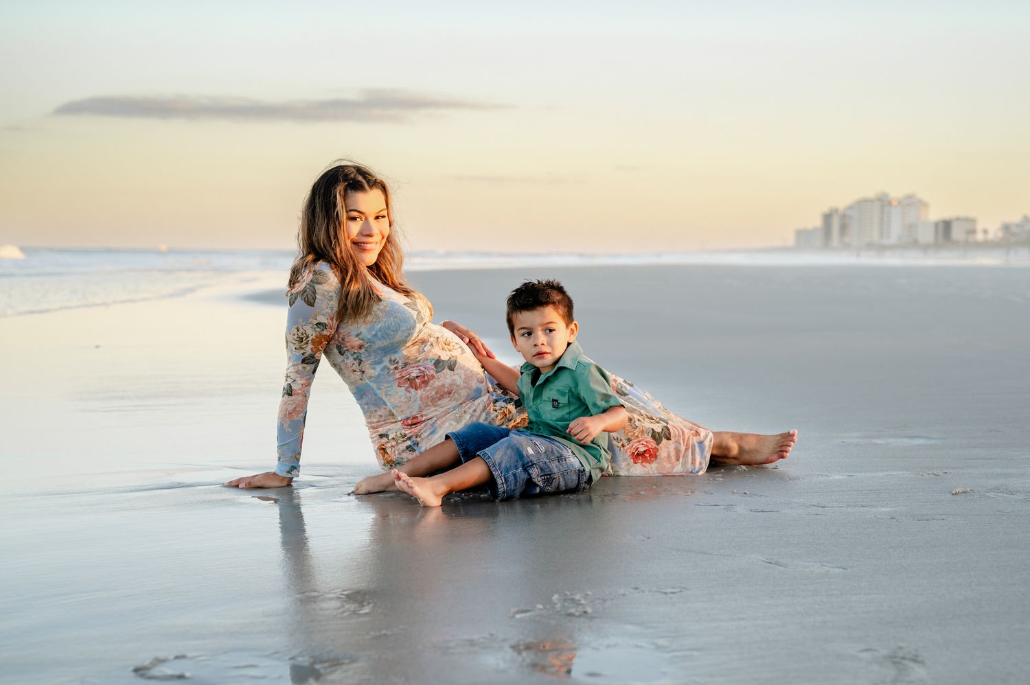 Pregnant woman and toddler boy sitting together at Jacksovnville Beach at sunset at a maternity photoshoot in Jacksonville, FL.