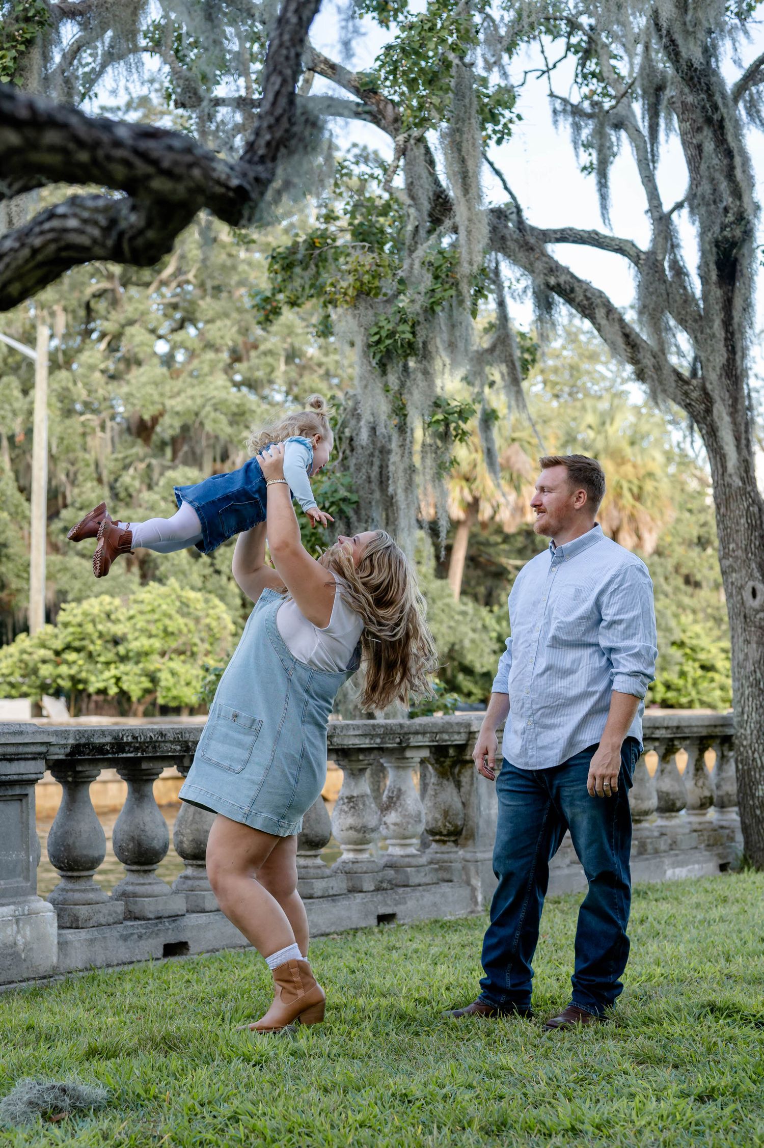 Playful family poses and dances on grassy lawn with Spanish moss hanging from trees in background.