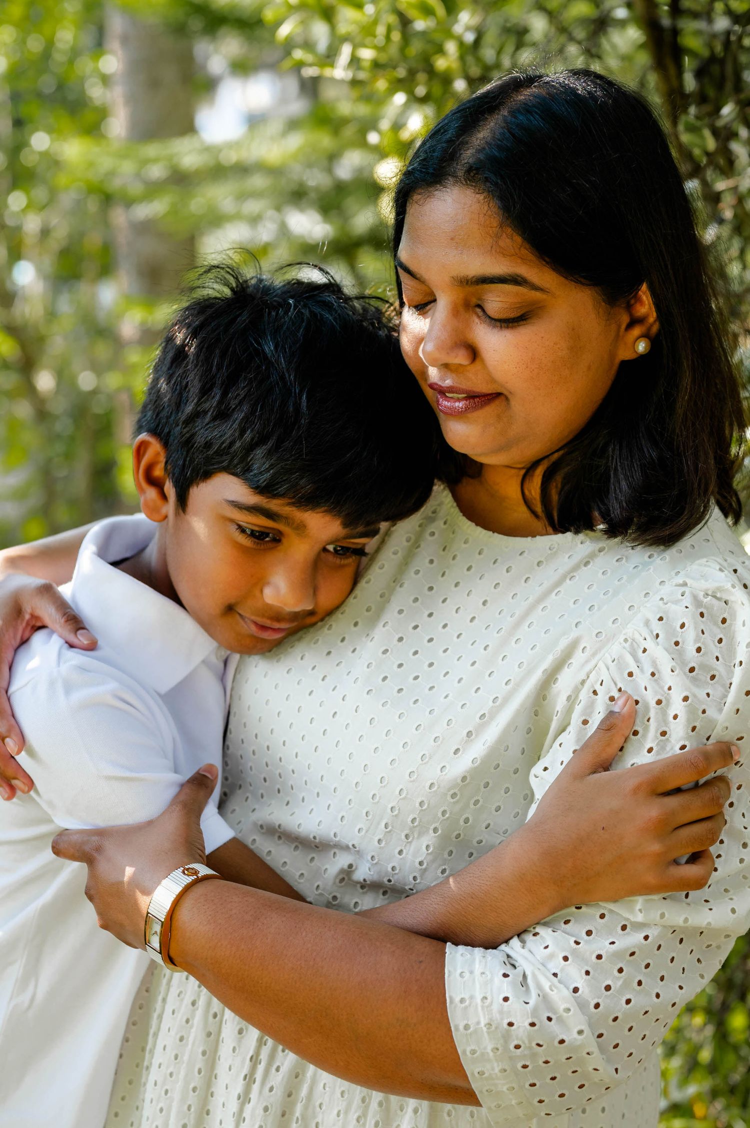 A tender embrace between two people wearing white outfits against a green outdoor background.
