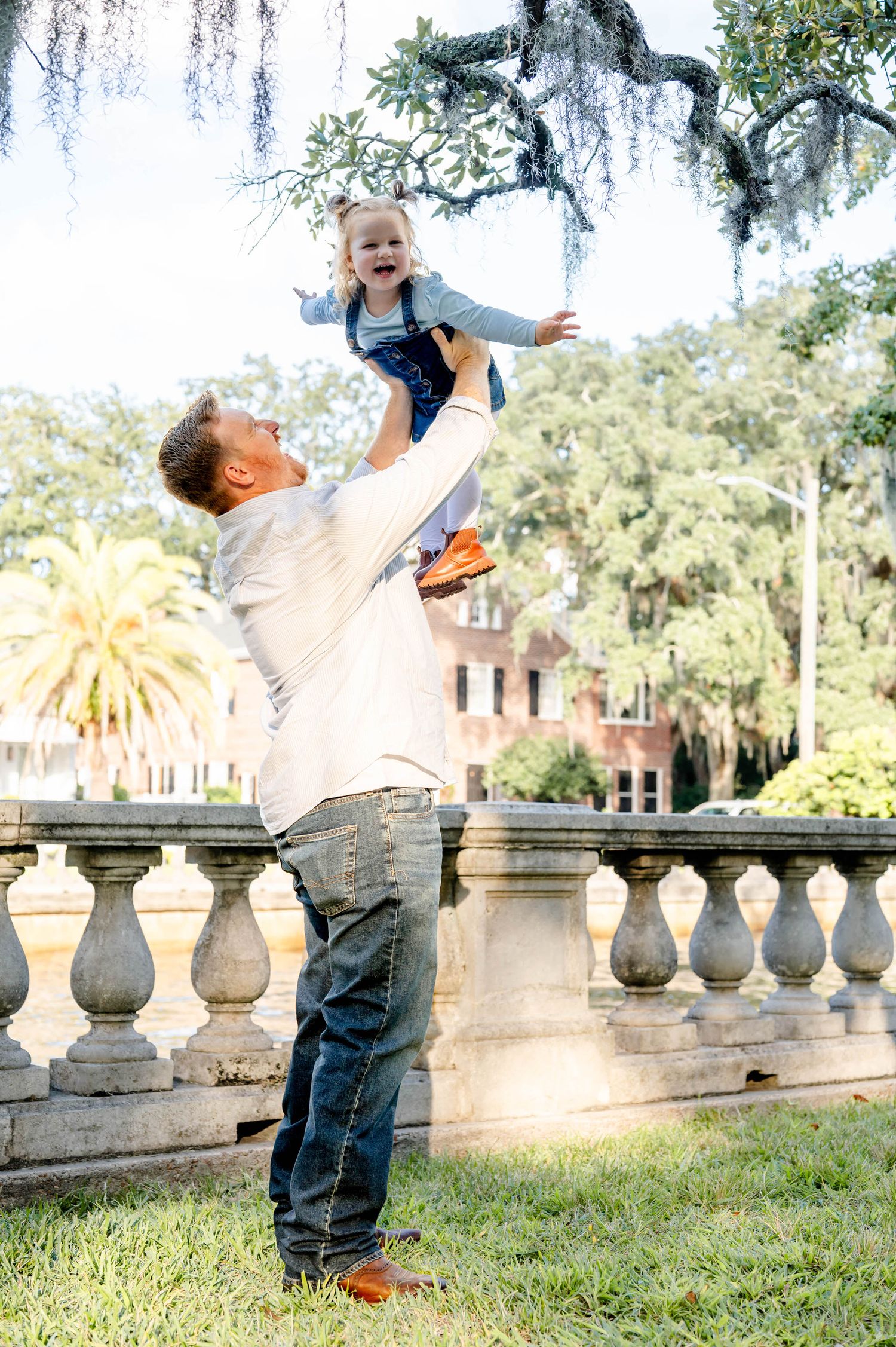 People share a joyful moment near an ornate stone balustrade with palm trees and historic architecture in background.