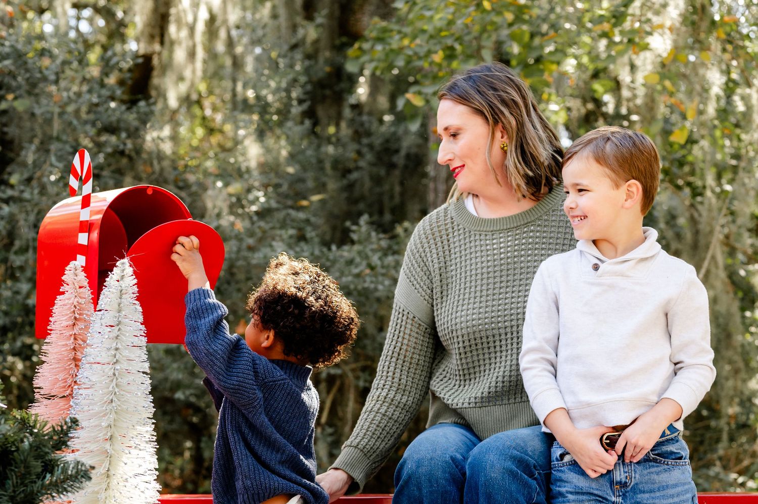 Family enjoying a winter photo session in a wooded area with festive holiday decorations and red accents.