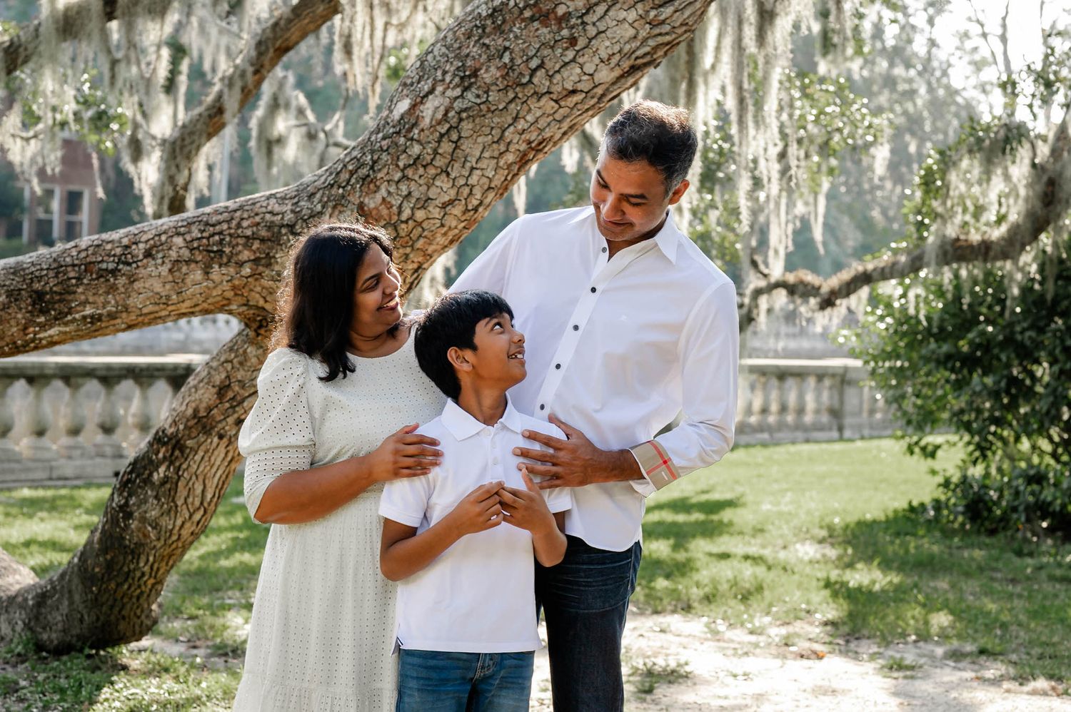 A family enjoys a tender moment together under a large oak tree with Spanish moss during a spring mini session in jacksonville, fl