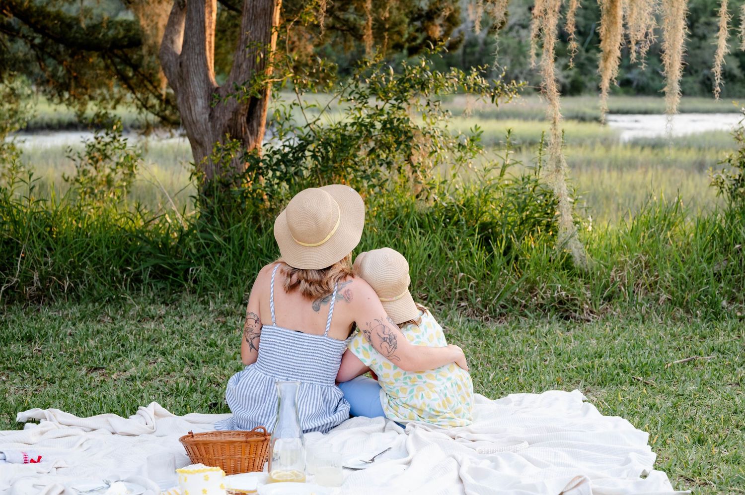 Mom and daughter family photoshoot - they are pictured in sun hats sitting on a picnic blanket in a Jacksonville park.