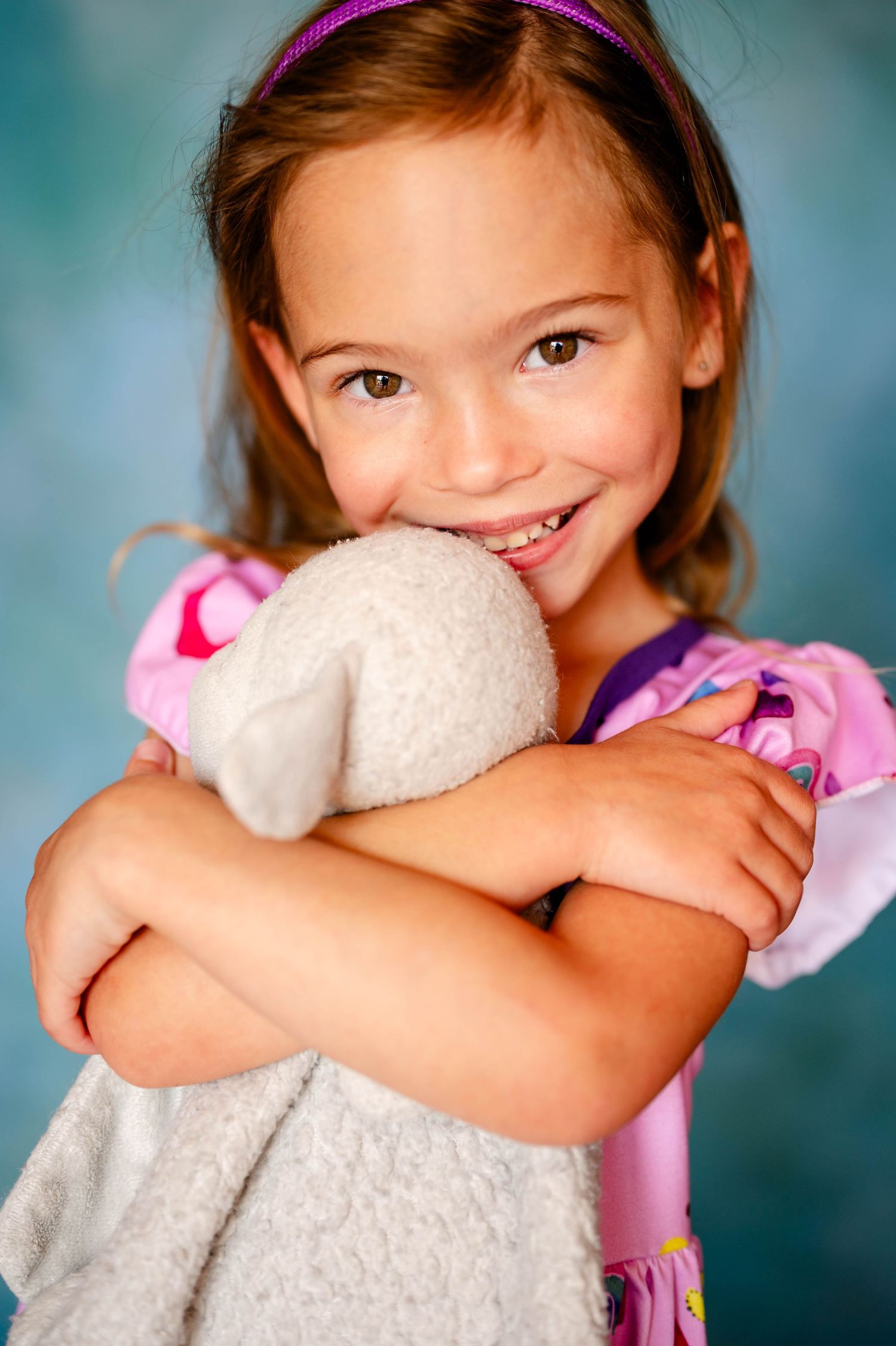 Young child hugging white teddy bear against blue background in a Jacksonville preschool photoshoot.