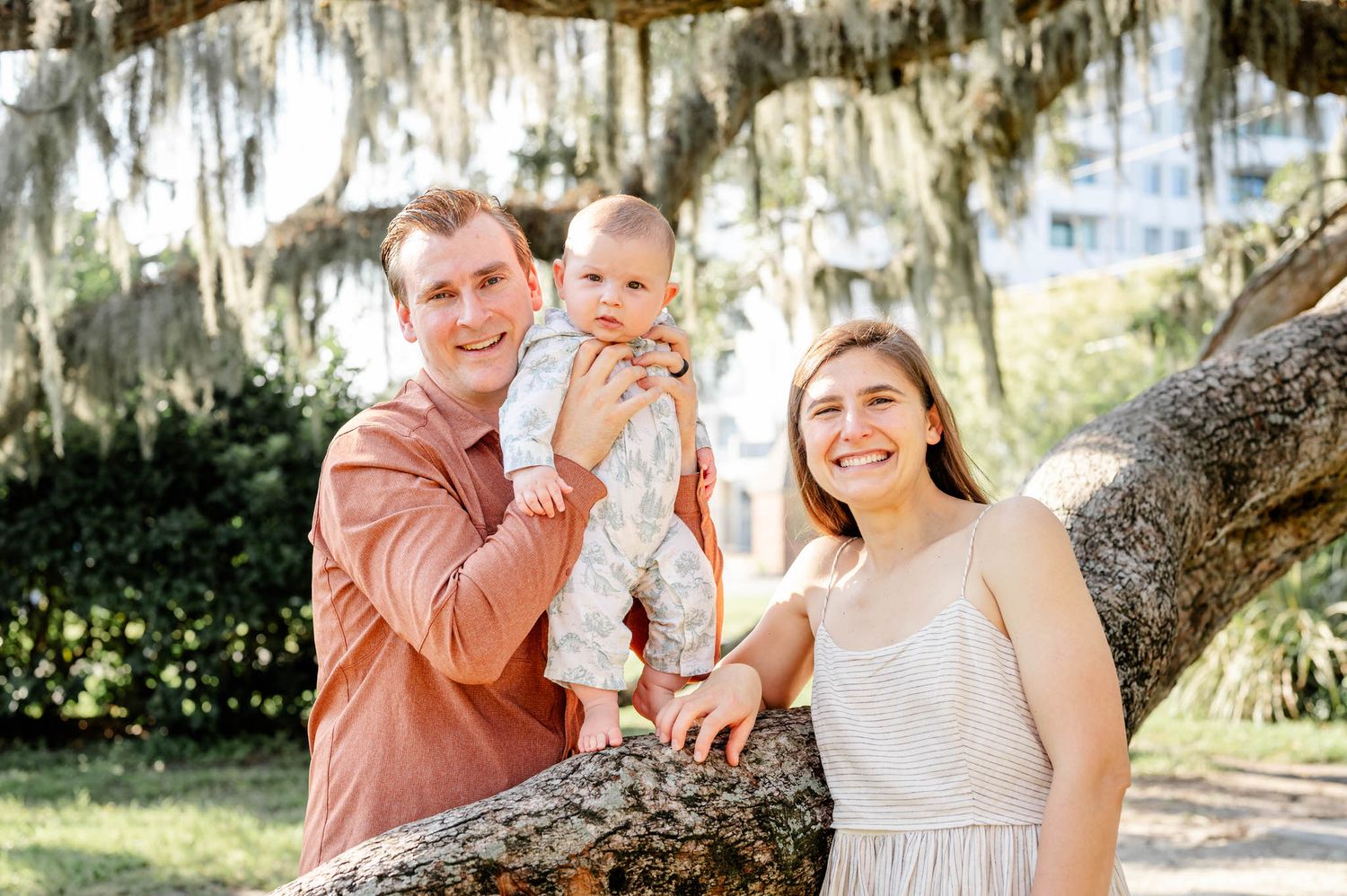 A family wearing peach and white outfits pose together under Spanish moss hanging from trees at a spring mini session in jacksonville, fl.