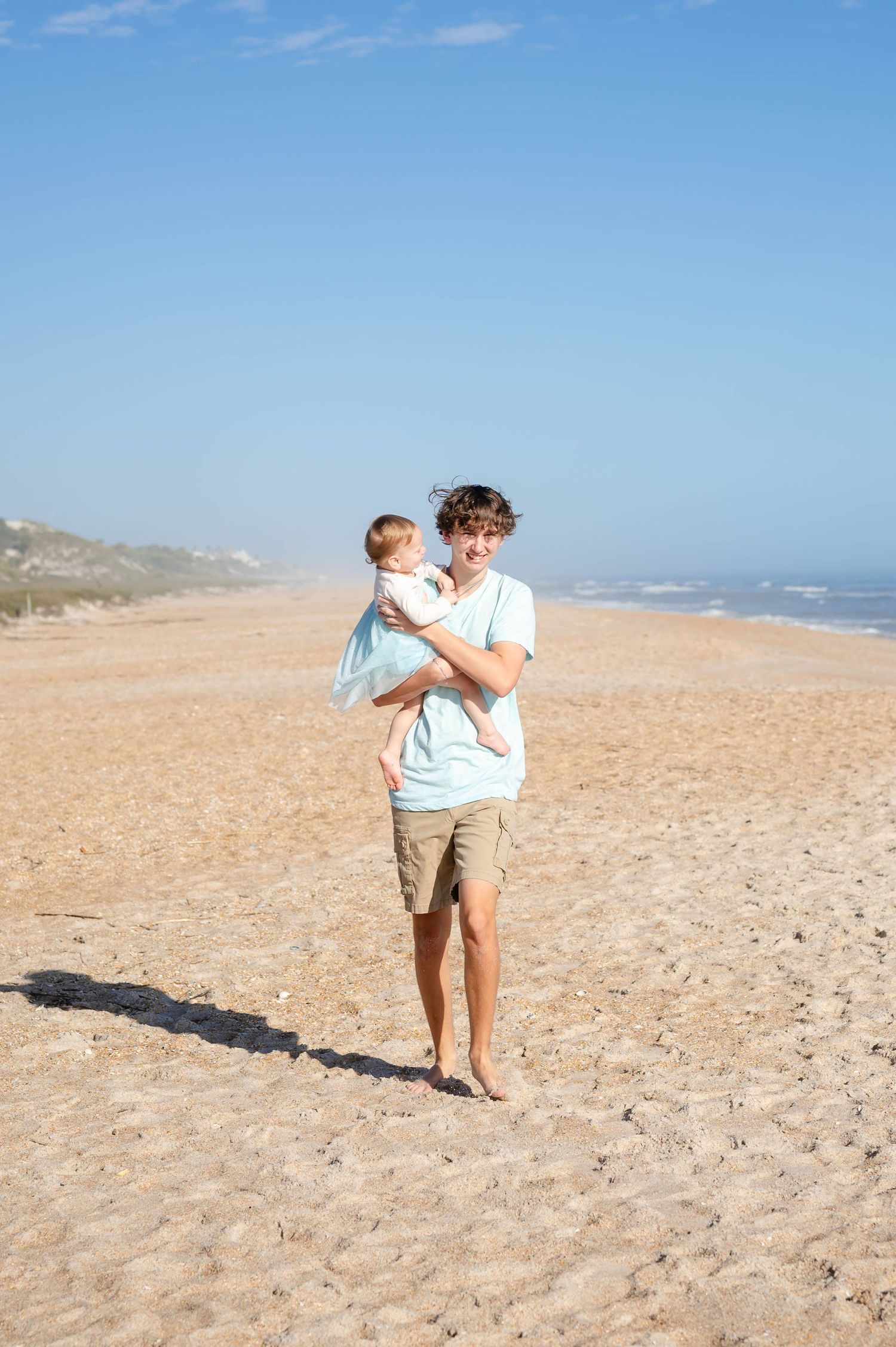 Family walking together on sandy beach on sunny summer day.