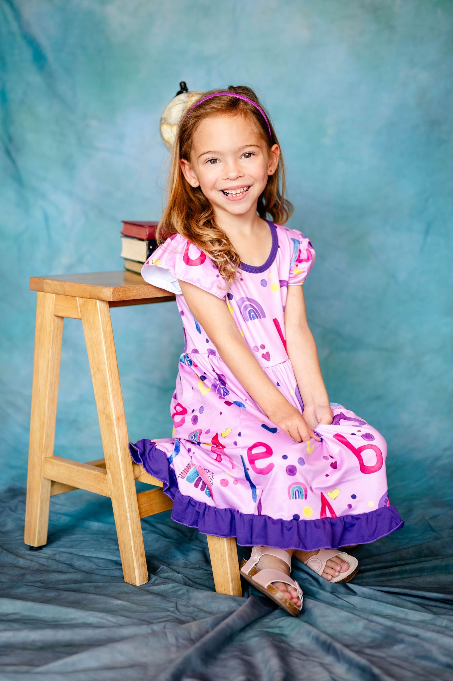 Preschool photographer in Jacksonville FL captured a child wearing pink and purple dress sitting on wooden stool.