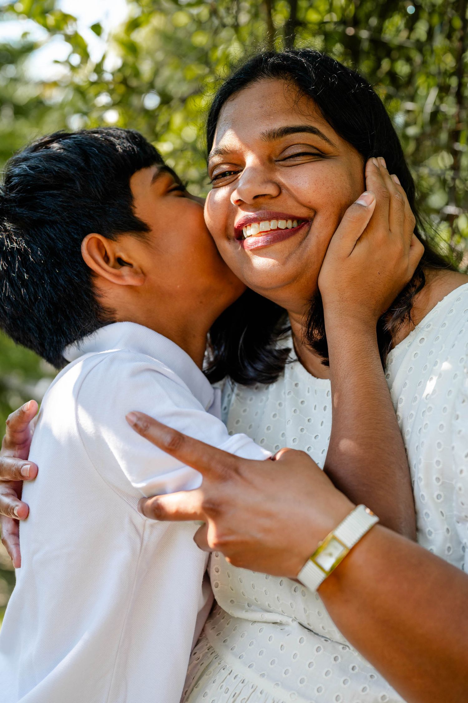 A tender moment captured outdoors as a child kisses his mom's cheek while both smile joyfully at a spring mini session in jacksonville, fl.