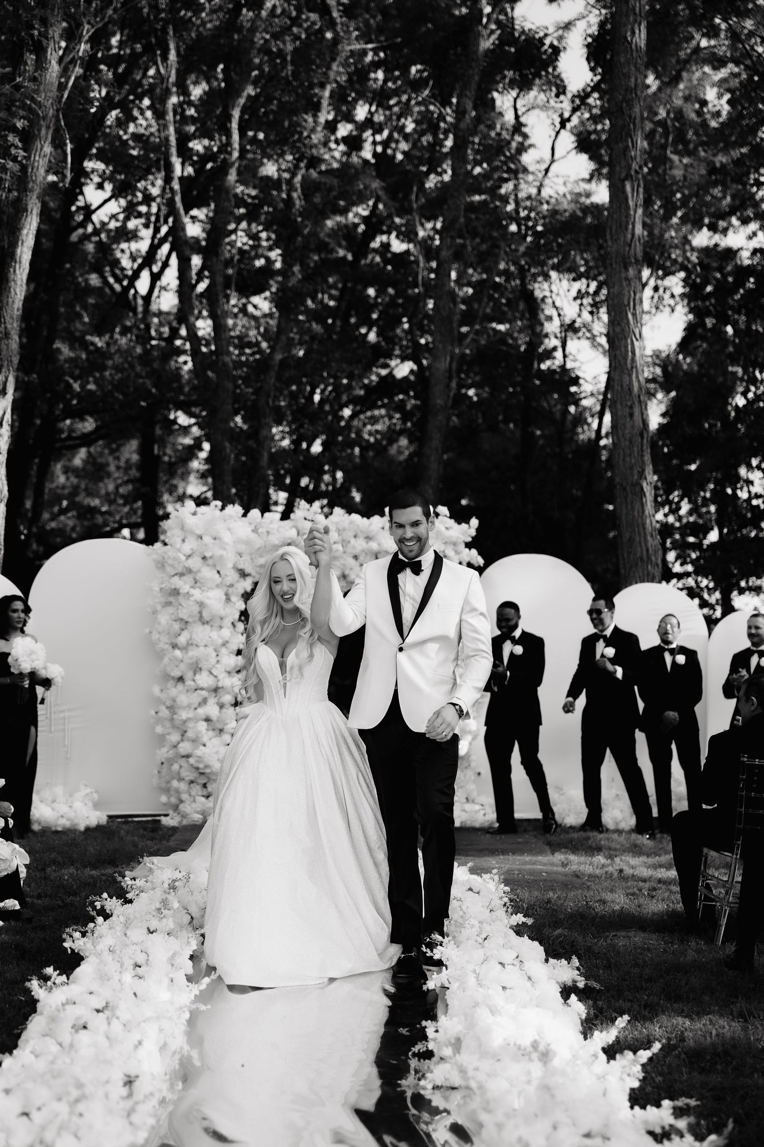 Wedding ceremony setup in a wooded outdoor setting with white floral arrangements and elegant decor.