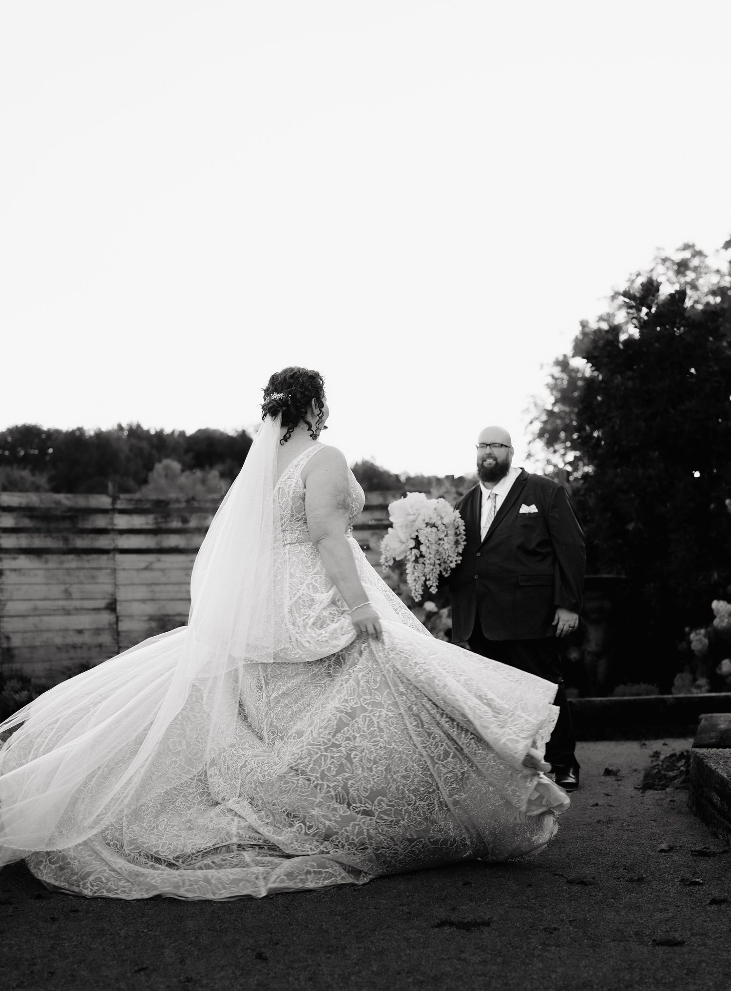 A flowing wedding dress train spreads elegantly across the ground in a dramatic black and white photo series.