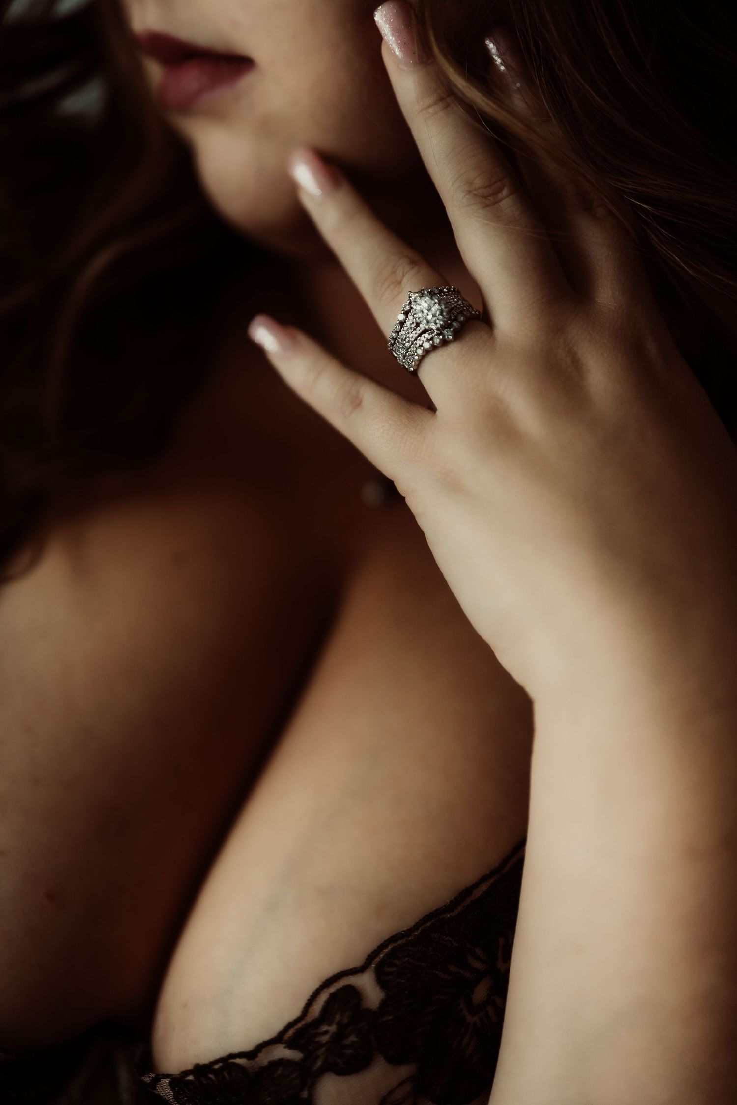 Close-up artistic photo of a hand wearing an elegant diamond engagement ring against a dark background.
