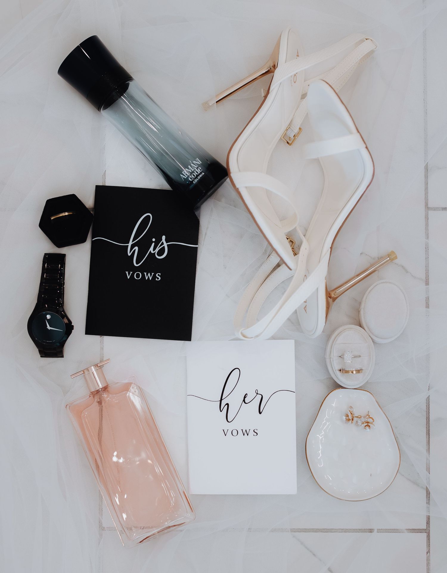 Wedding details flatlay with black and pink perfume bottles, white cards, and delicate accessories on light background.