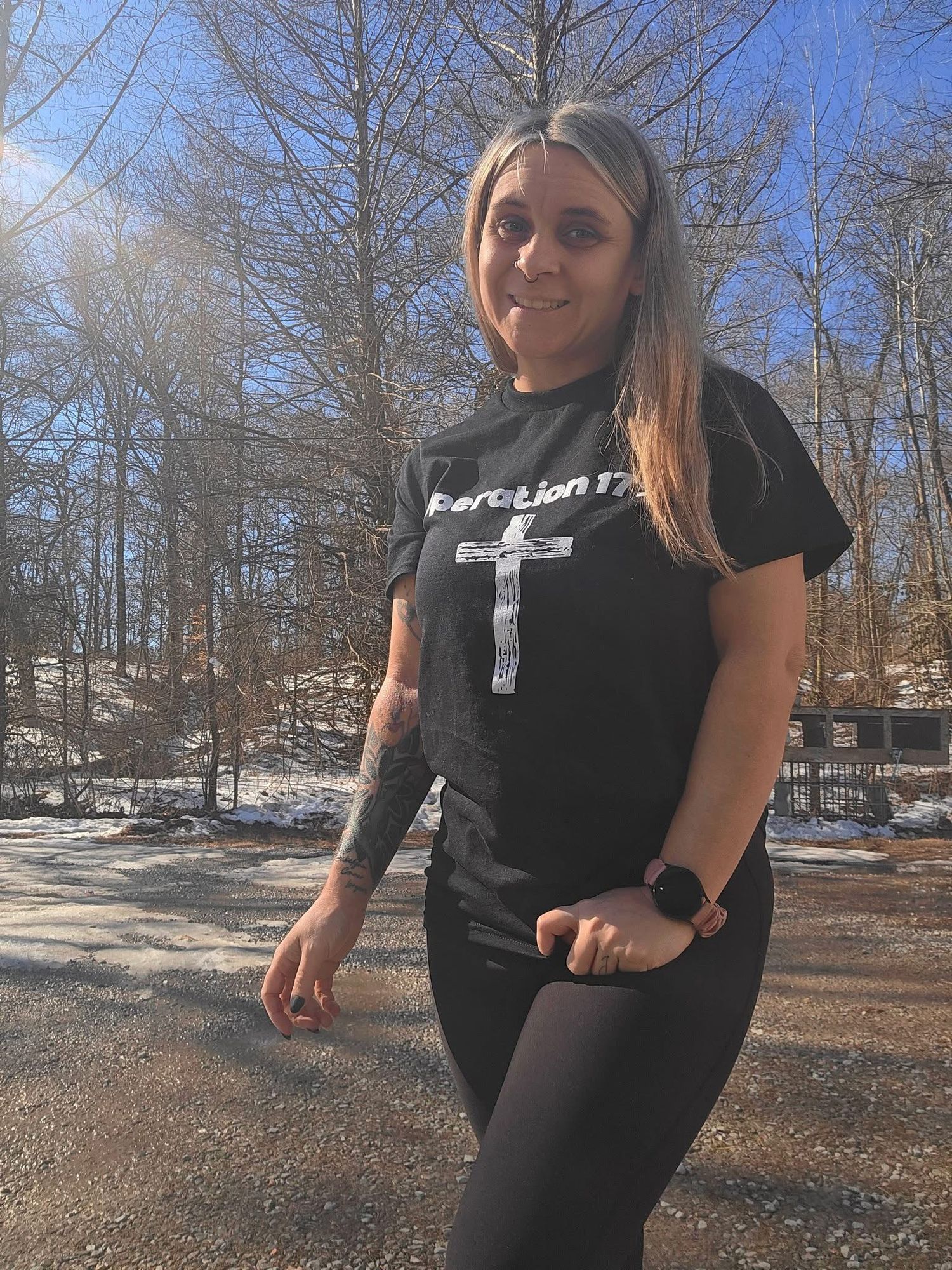 Person in black workout attire demonstrates stretching exercises outdoors in a wooded winter setting.