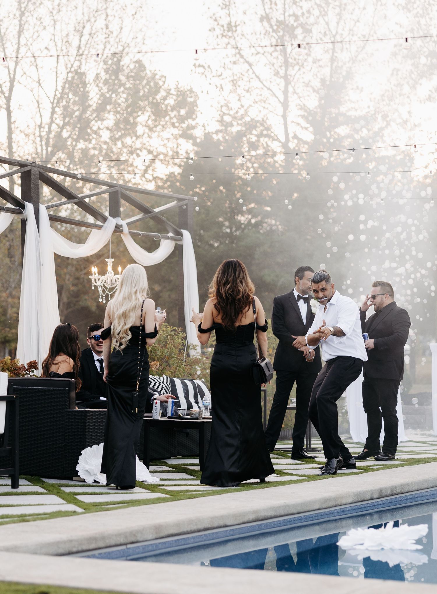 Wedding guests mingle and socialize around an outdoor swimming pool during an elegant evening reception.