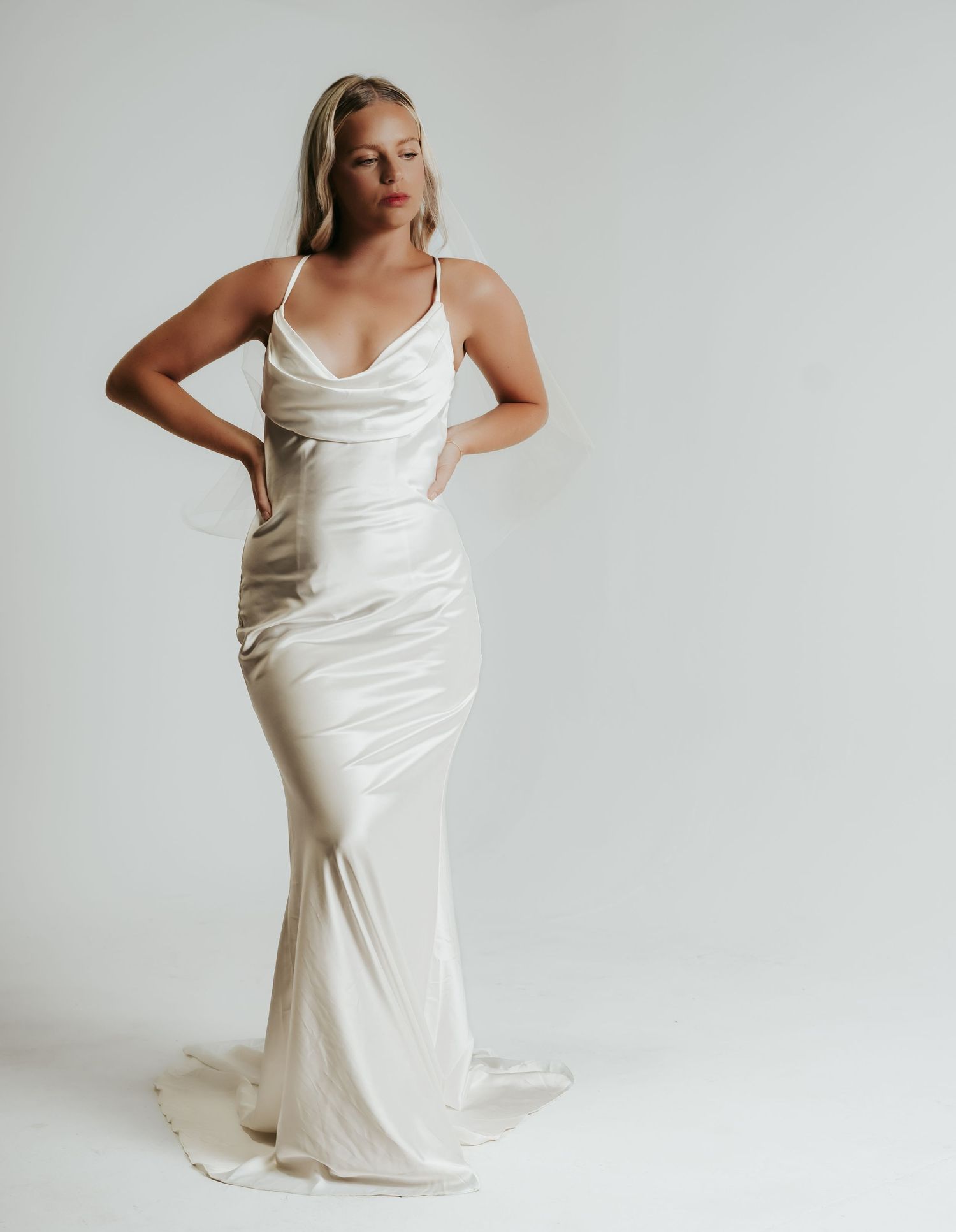 Woman wearing an ivory satin cowl neck slip wedding gown with spaghetti straps and a flowing train.