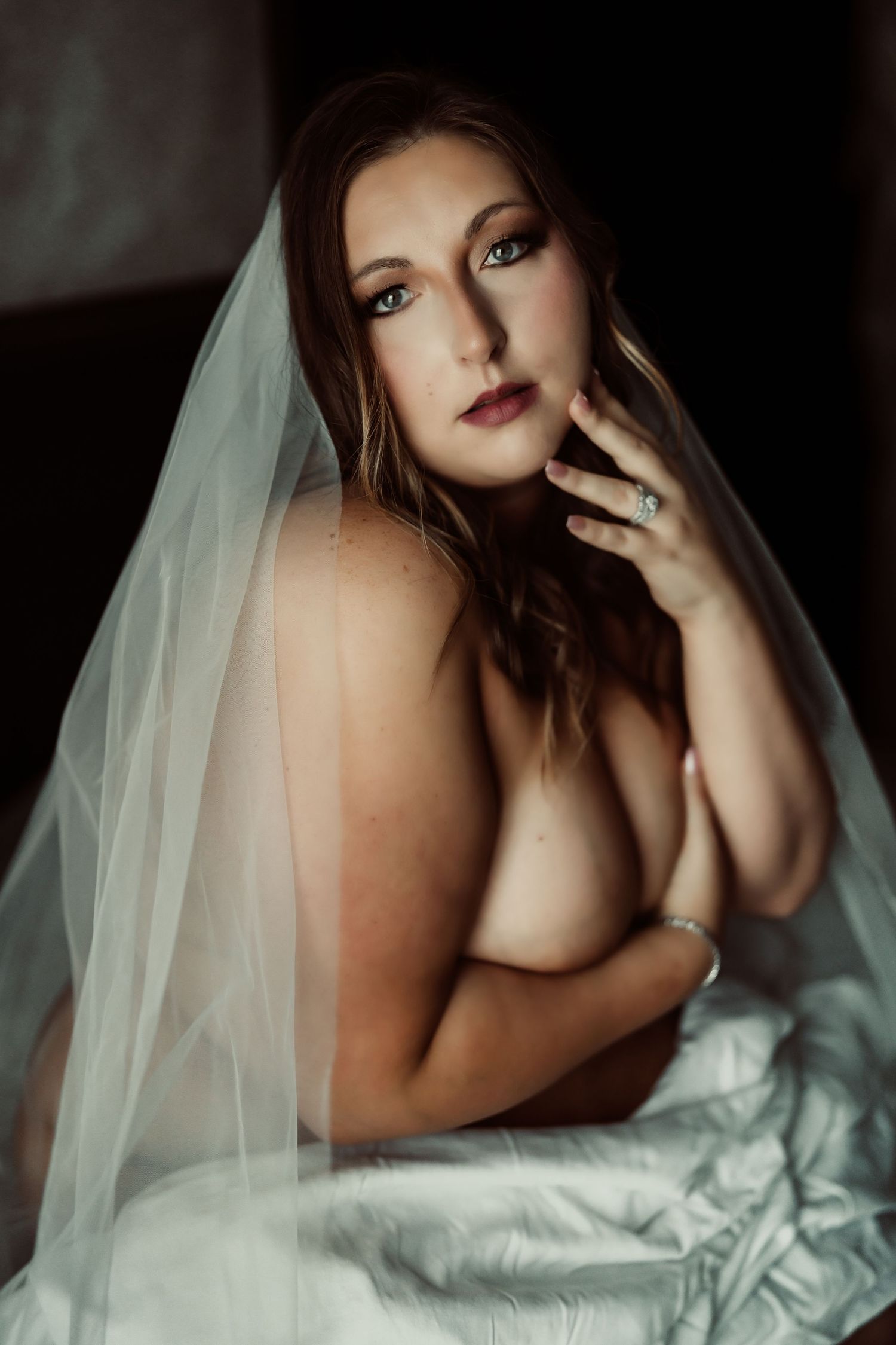 Artistic boudoir photography series showing intimate poses with white bedding and veil in moody lighting.