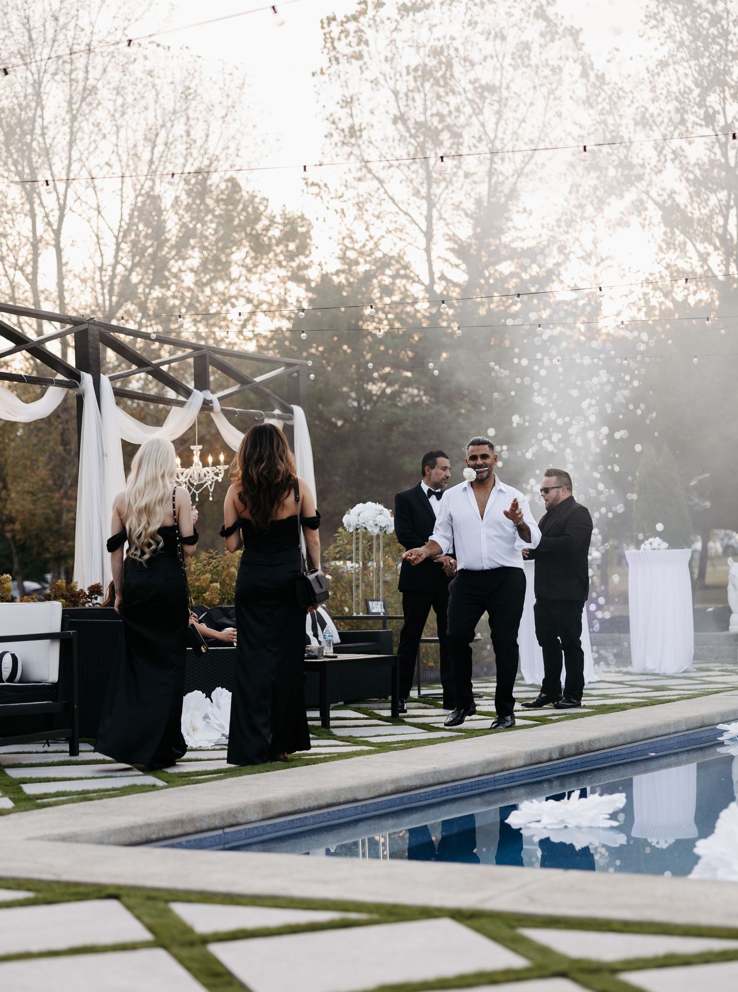A modern outdoor wedding ceremony setup with guests gathered around a sleek reflecting pool at sunset.