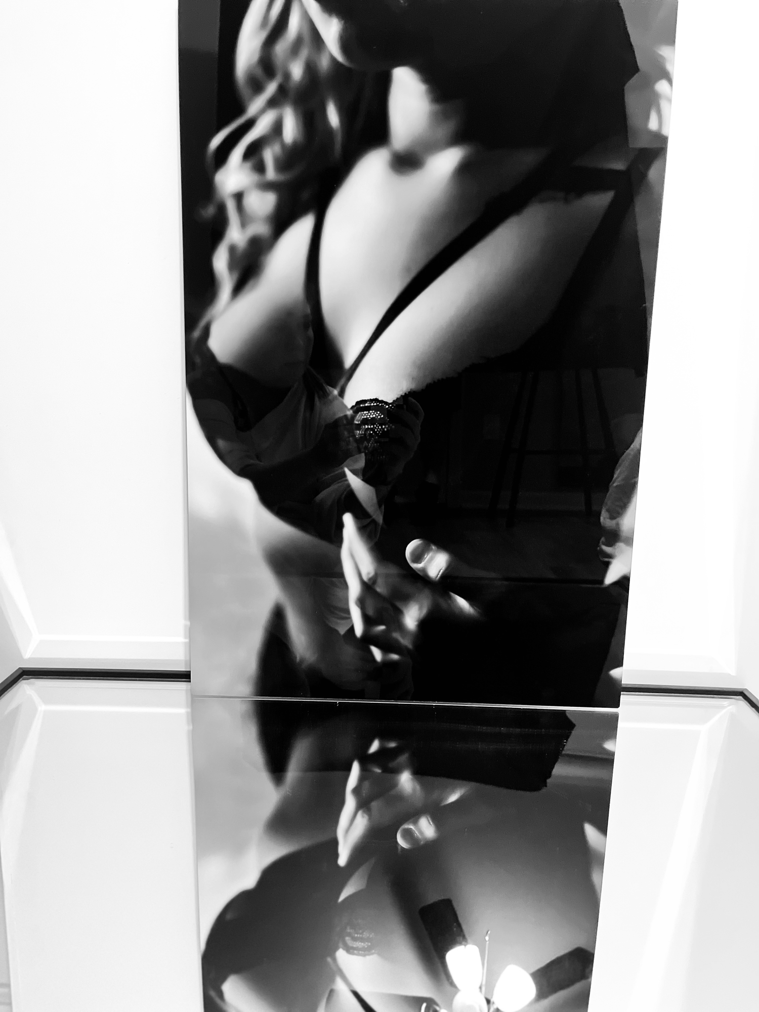Black and white mirror selfie of a woman in black lace lingerie with dramatic light and shadow reflections.