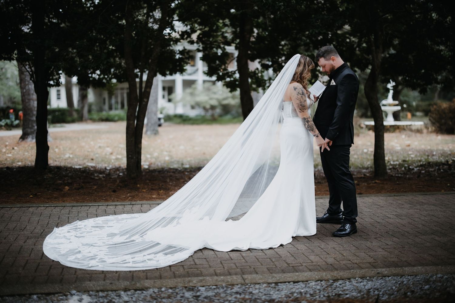A romantic wedding couple shares an intimate moment outdoors while the bride's long white veil flows behind them.