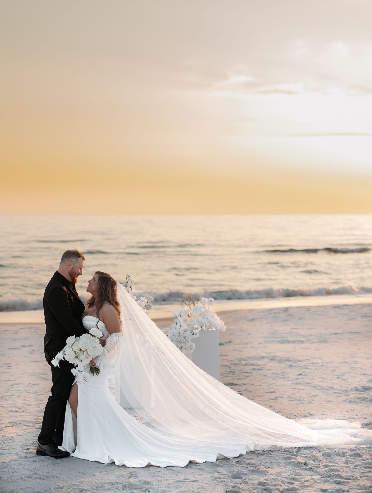 A romantic beach wedding photoshoot with a flowing white dress and dramatic sunset over the ocean waves.