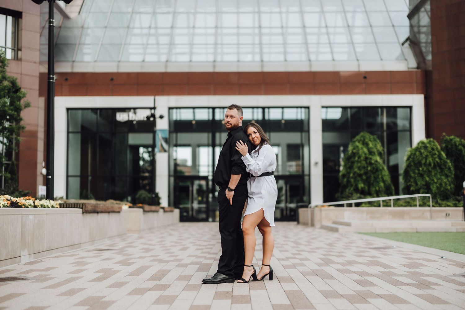A couple shares romantic moments across multiple scenes at a modern building with glass and stone architecture.