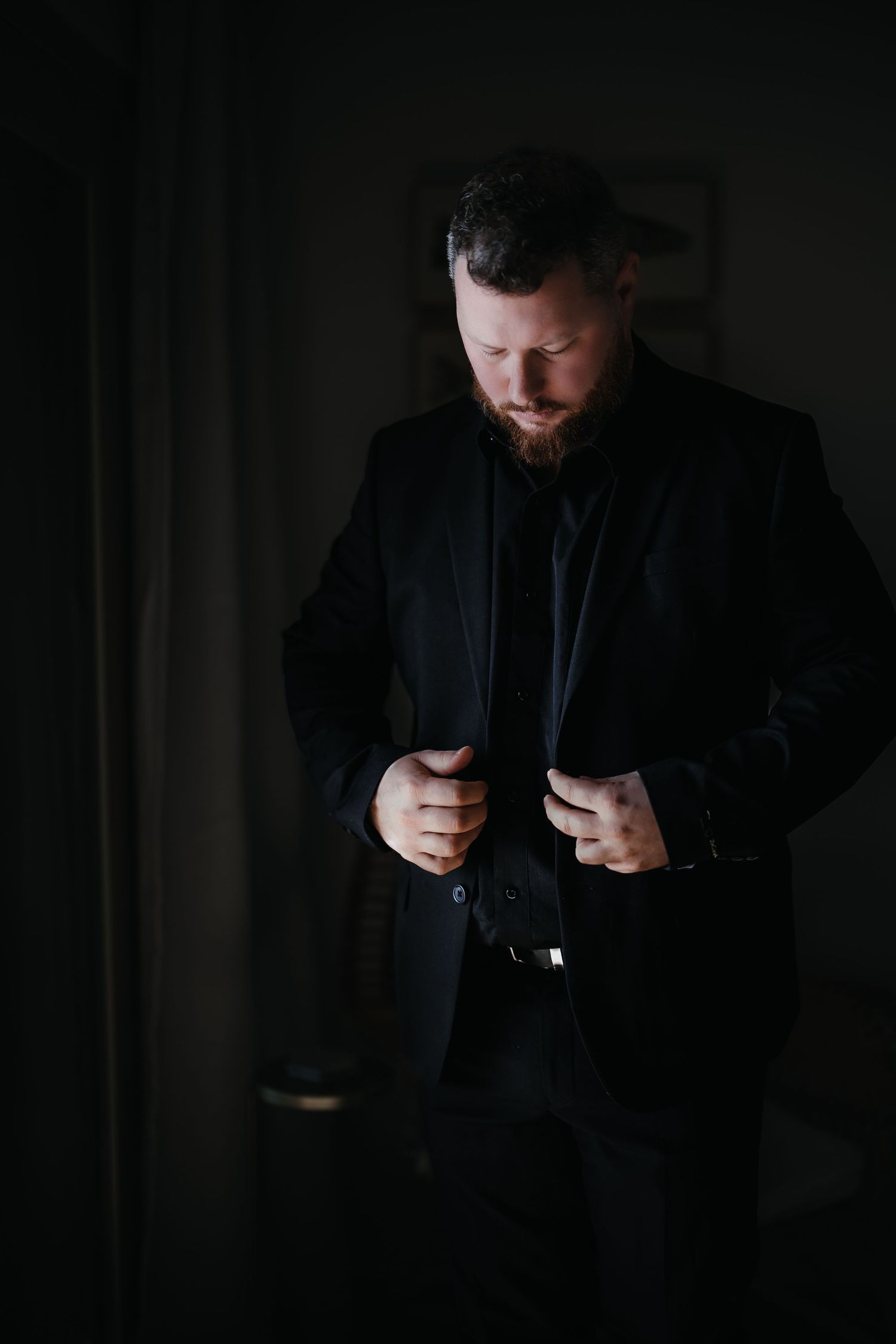 A person in dark clothing illuminated by soft light looks down at a mobile phone screen in a dimly lit setting.