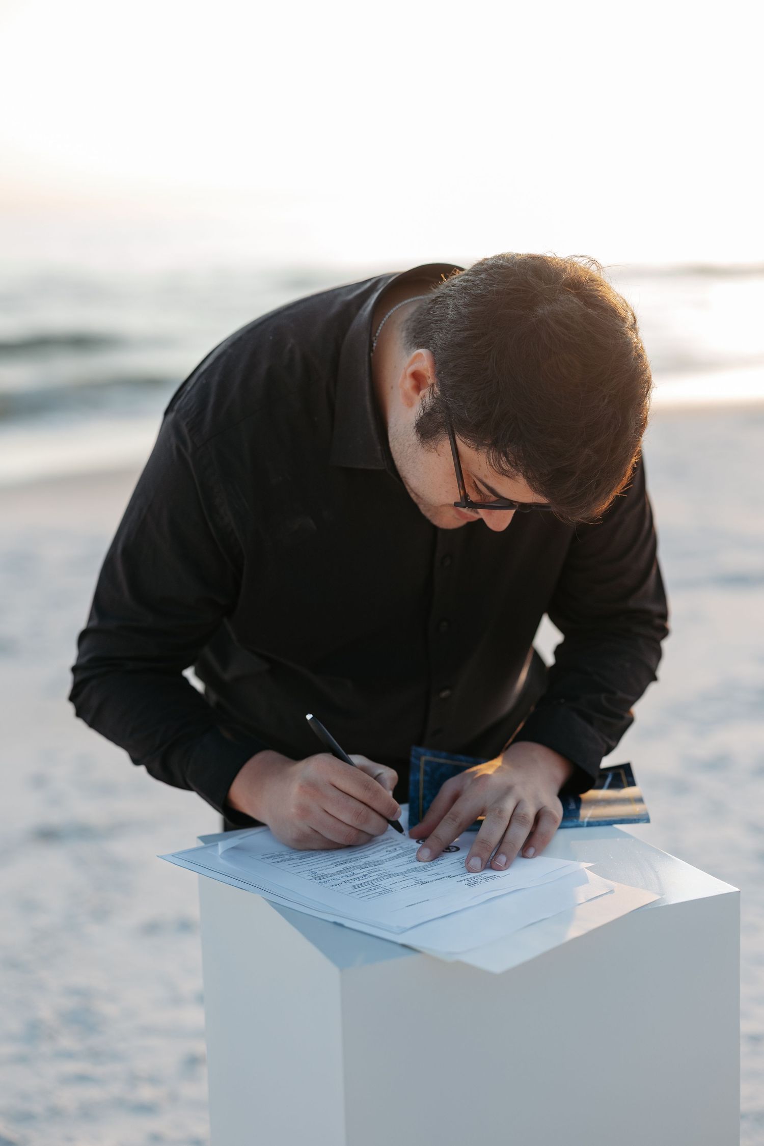 Person in black clothing writing or drawing on white paper while leaning over a white surface in a series of photos.