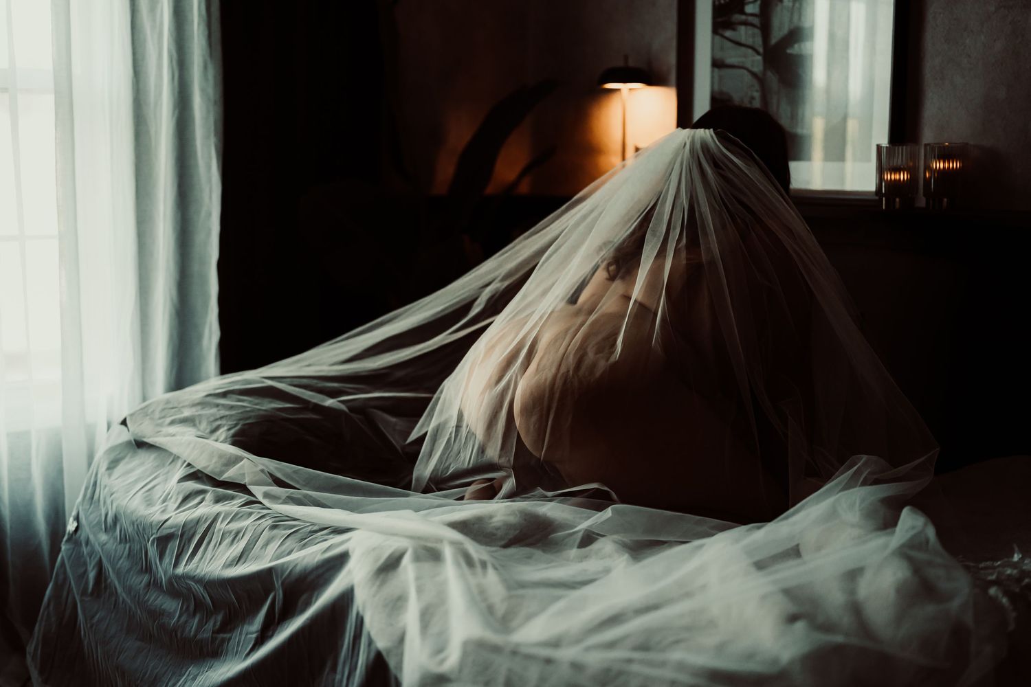 A dark and moody image shows white flowing fabric or curtains illuminated by dramatic lighting against a black background.