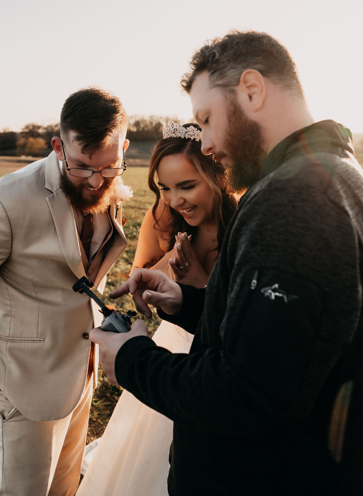 A wedding couple and officiant share a joyful moment of laughter during an outdoor sunset ceremony.