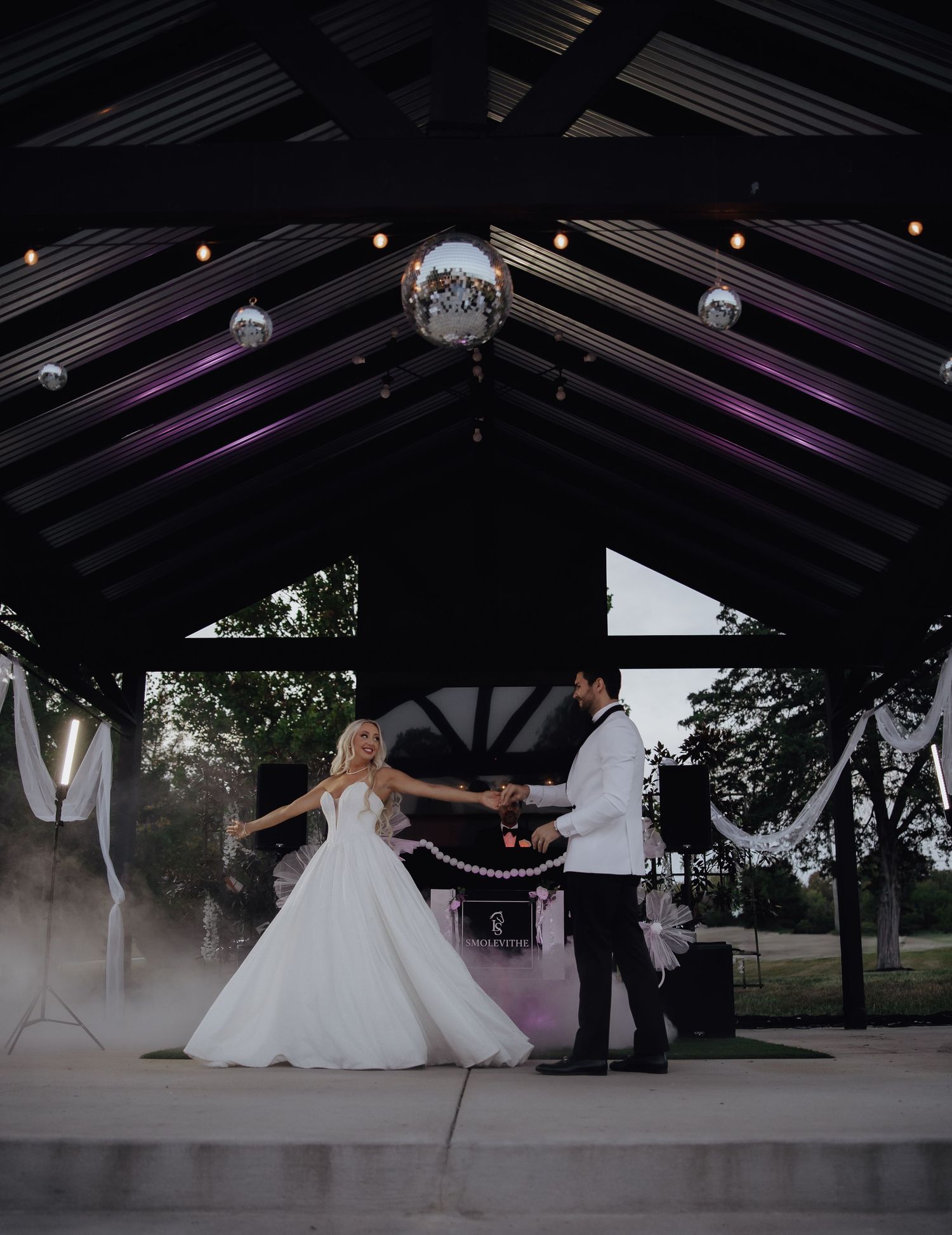 Wedding reception venue with purple lighting and disco balls hanging from dark wooden beams.