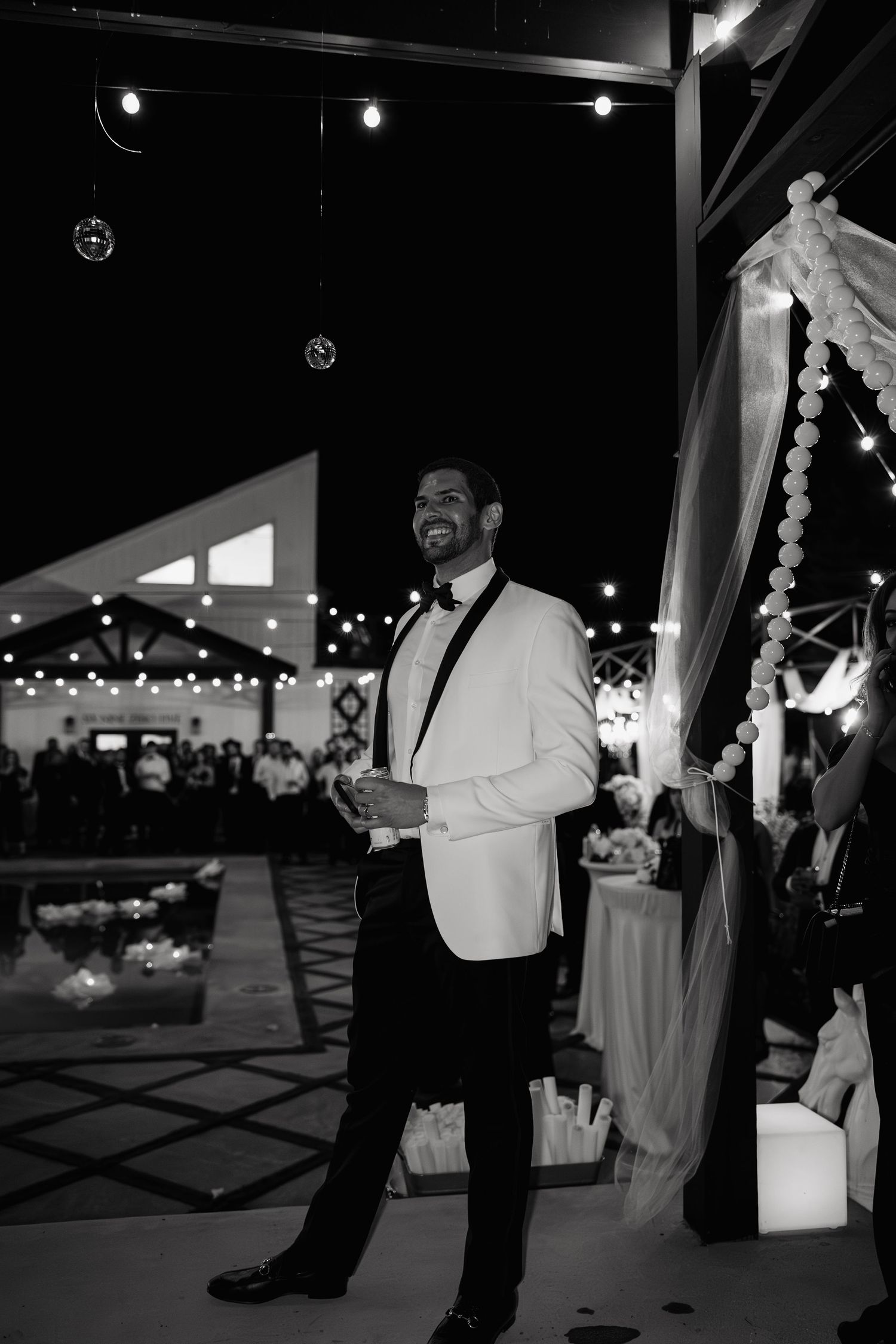 Black and white photo of wedding guests dancing and celebrating in an elegant indoor venue.