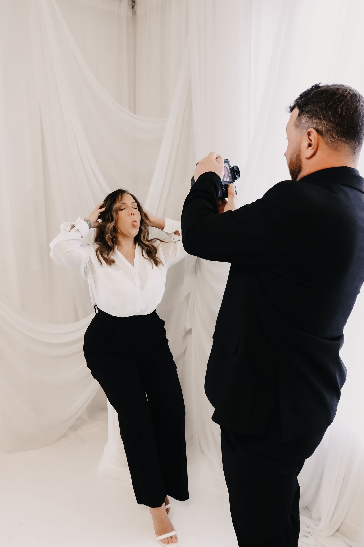 Two people in black outfits dance and pose together against a white curtain backdrop in a photo series.