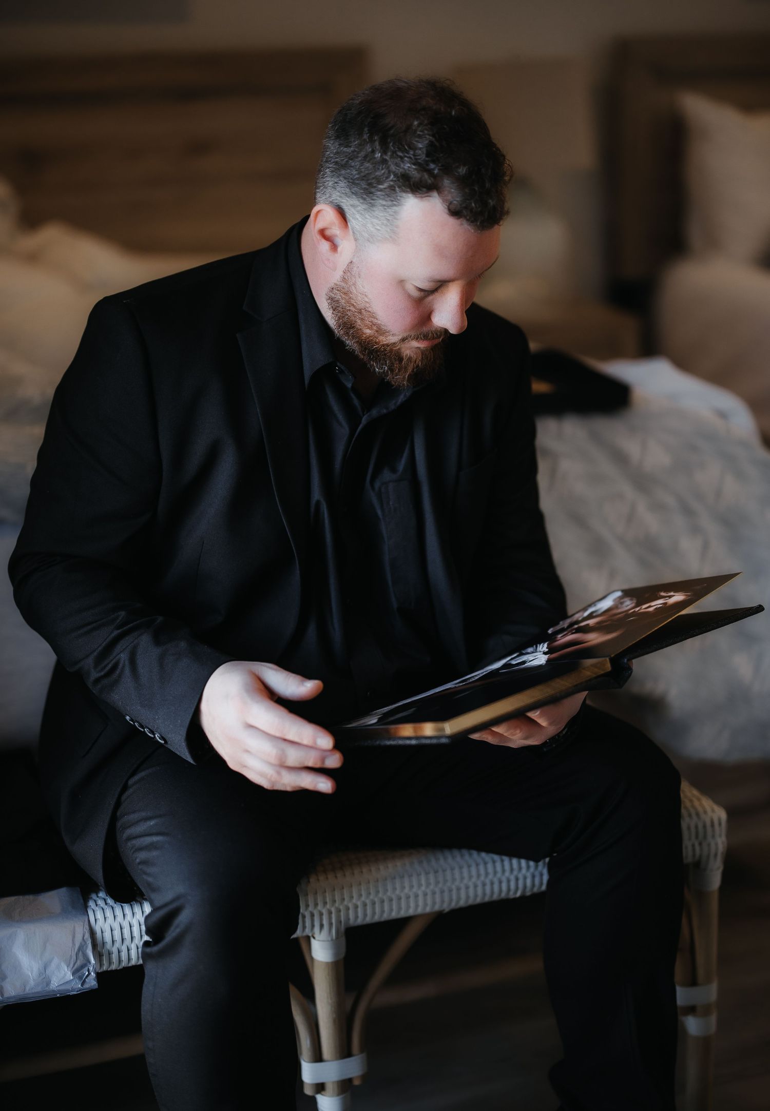 A person in black clothing sits on a couch while looking down at a digital tablet device in a dimly lit room.