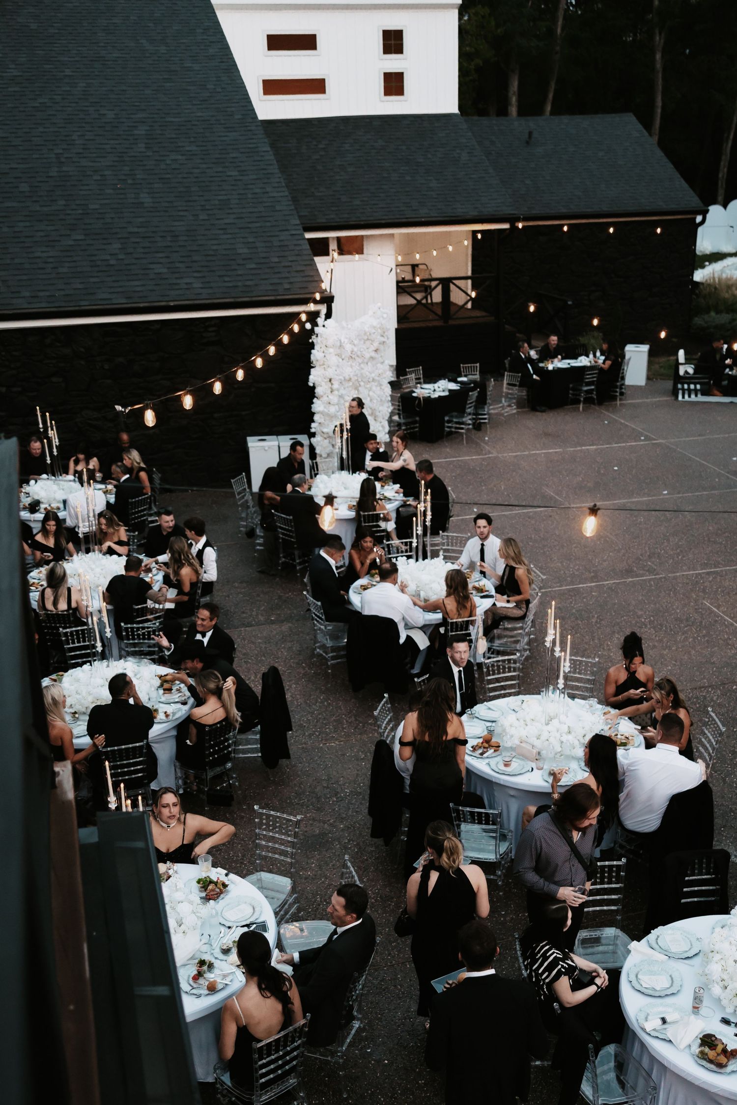 Elegant outdoor wedding reception at dusk with string lights illuminating tables of guests dining under the evening sky.
The Hillside Estate