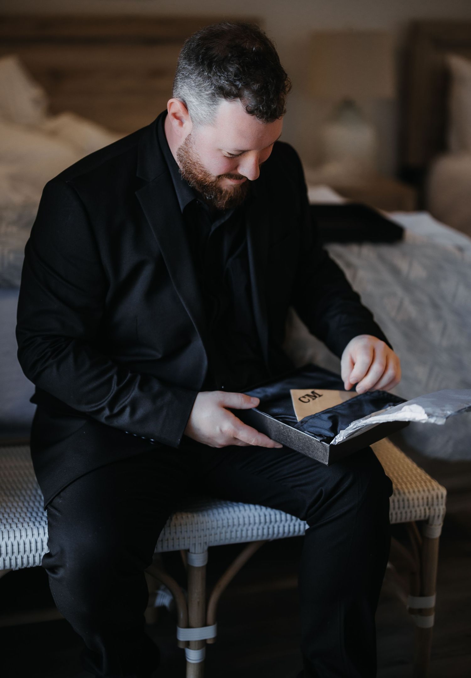 A person in a black sweater sits on a couch while looking down at something in their hands.