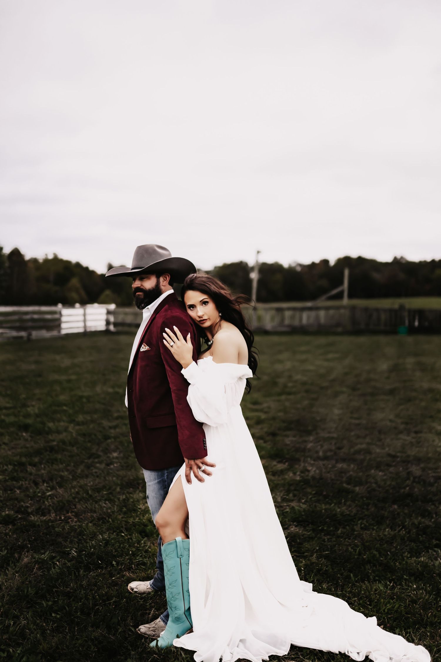 A couple embraces in a field while wearing a white dress and cowboy boots.
