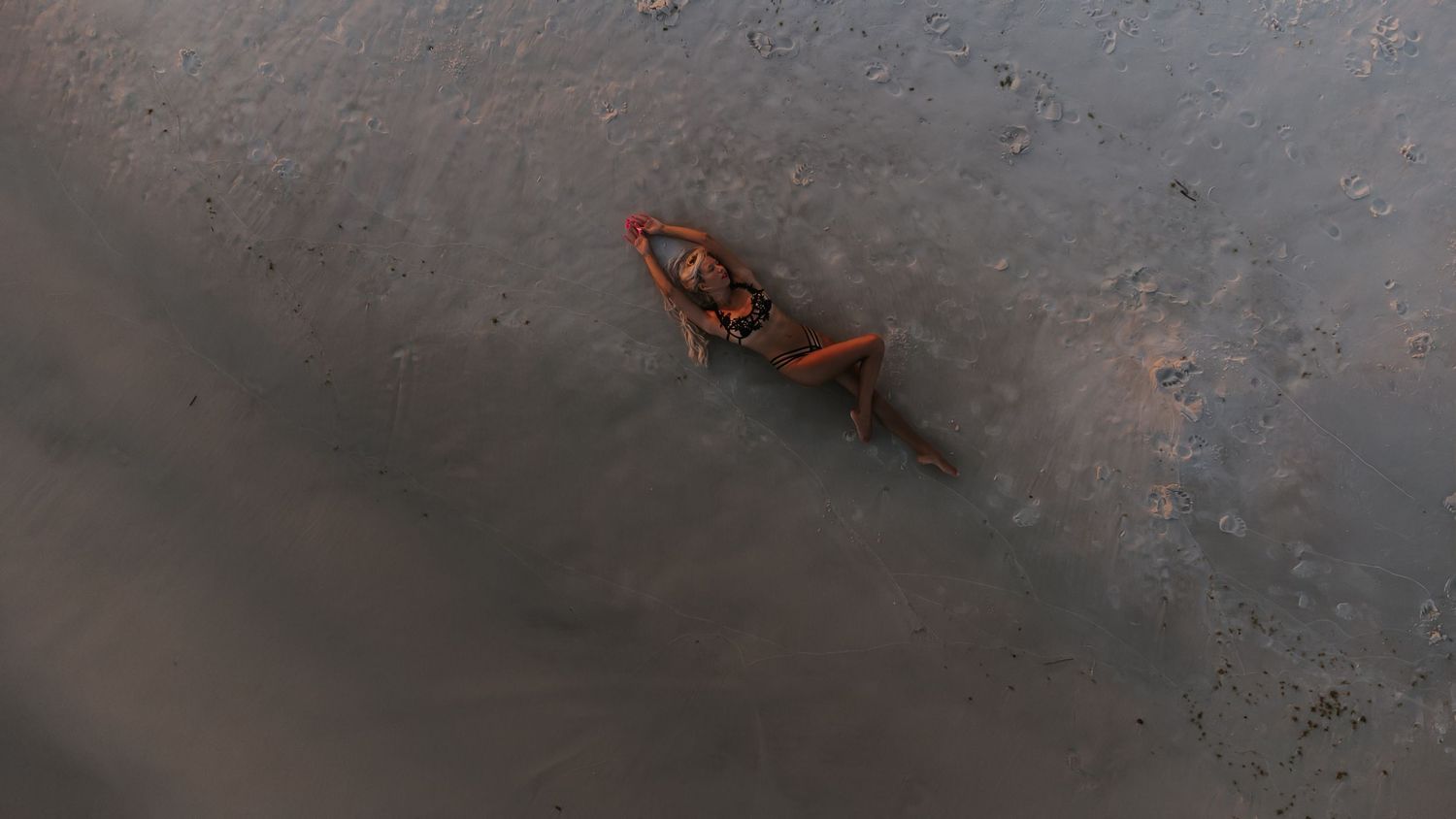 Aerial view of a red kayak paddling through calm, murky brown waters seen from above.