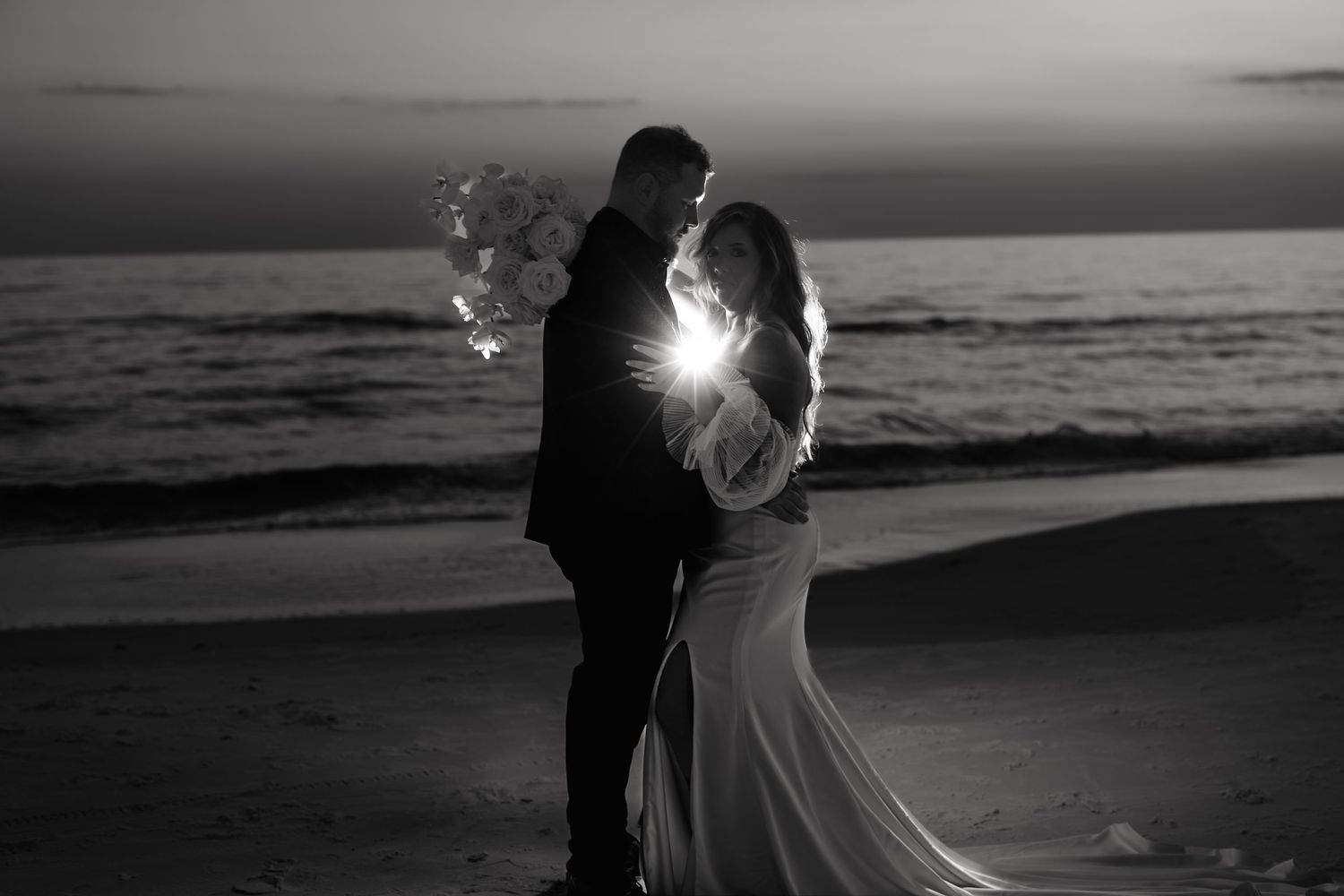 A romantic silhouette of a couple embracing on the beach at sunset with light glowing between them in black and white.
Villa Woodbine