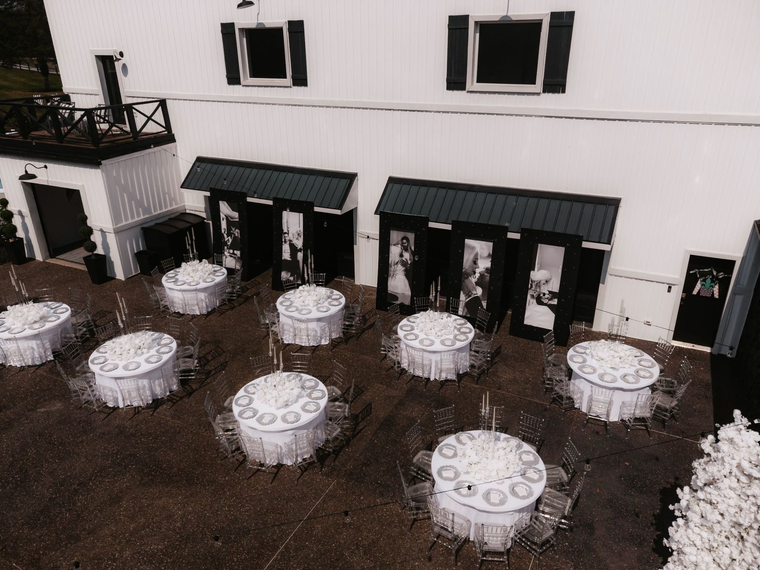 White round tables with tablecloths are arranged in rows on a dark floor in an indoor venue.