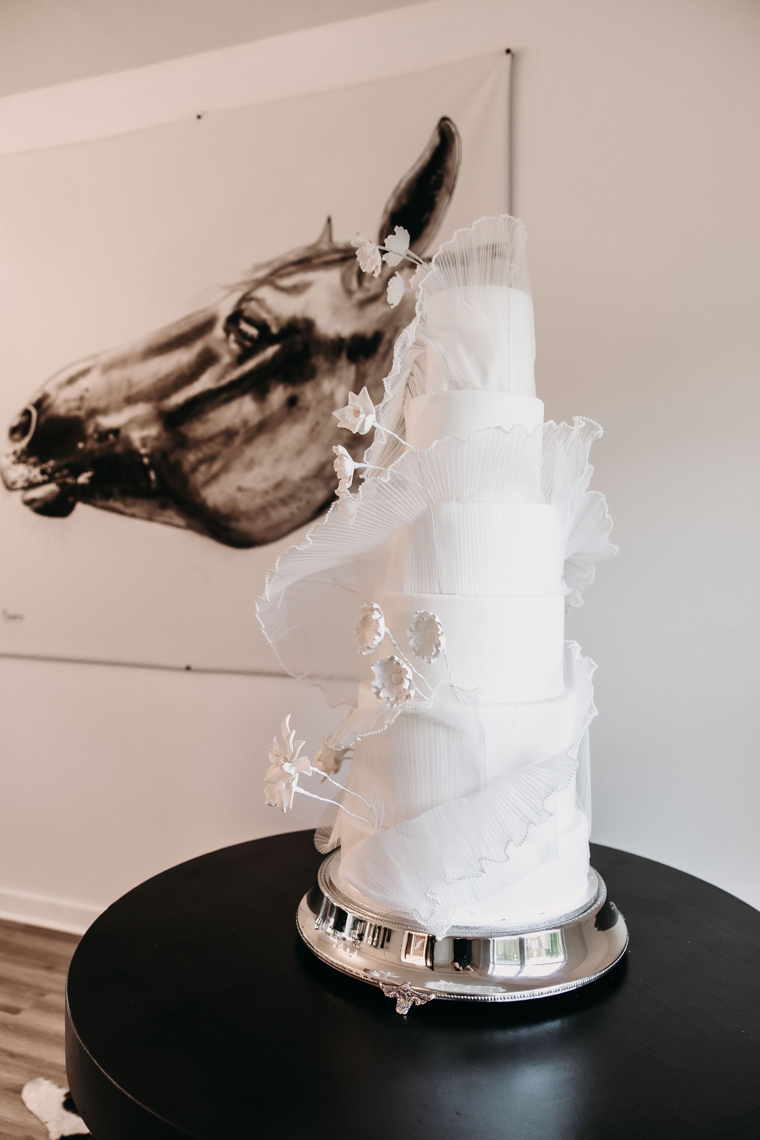 Three white wedding cakes displayed on black platforms with delicate sugar work decorations and elegant tiers.
