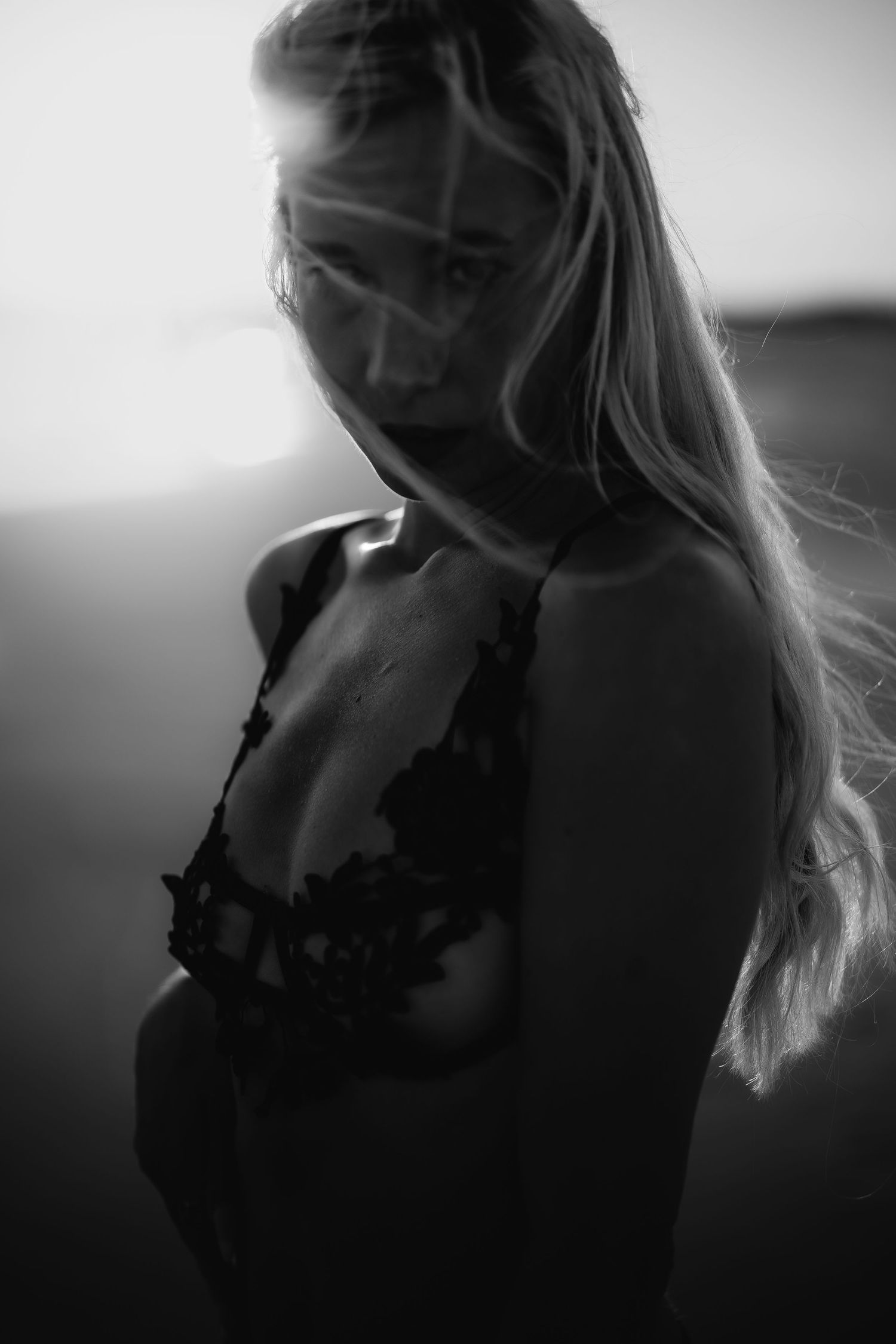 Black and white portrait of a blonde woman in lace lingerie posing in soft backlight.