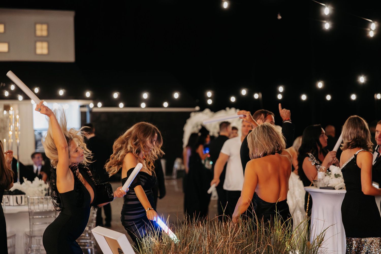 Wedding guests dancing and celebrating on an outdoor dance floor illuminated by string lights at night.