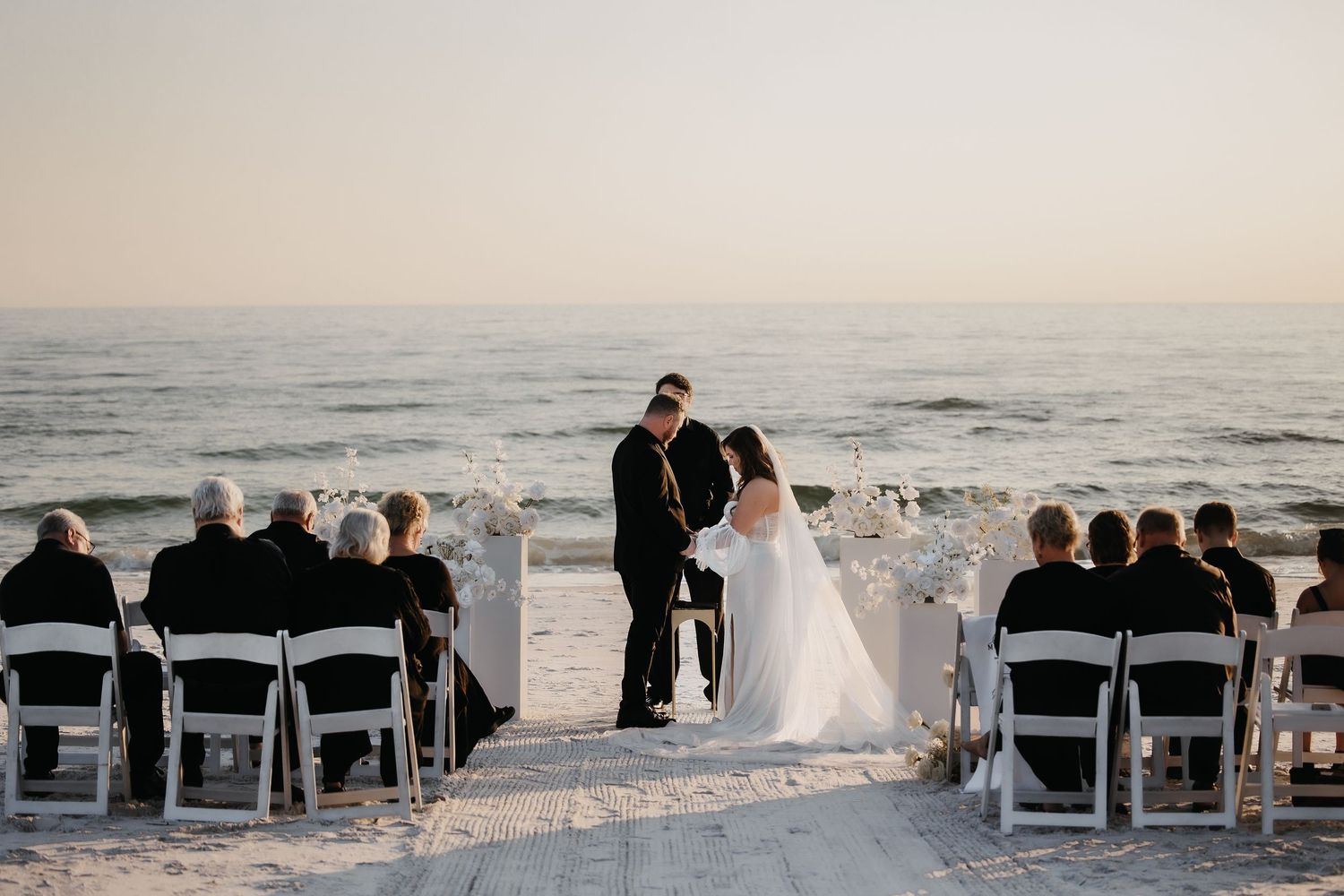 A beach wedding ceremony setup with white chairs facing the ocean at sunset.
