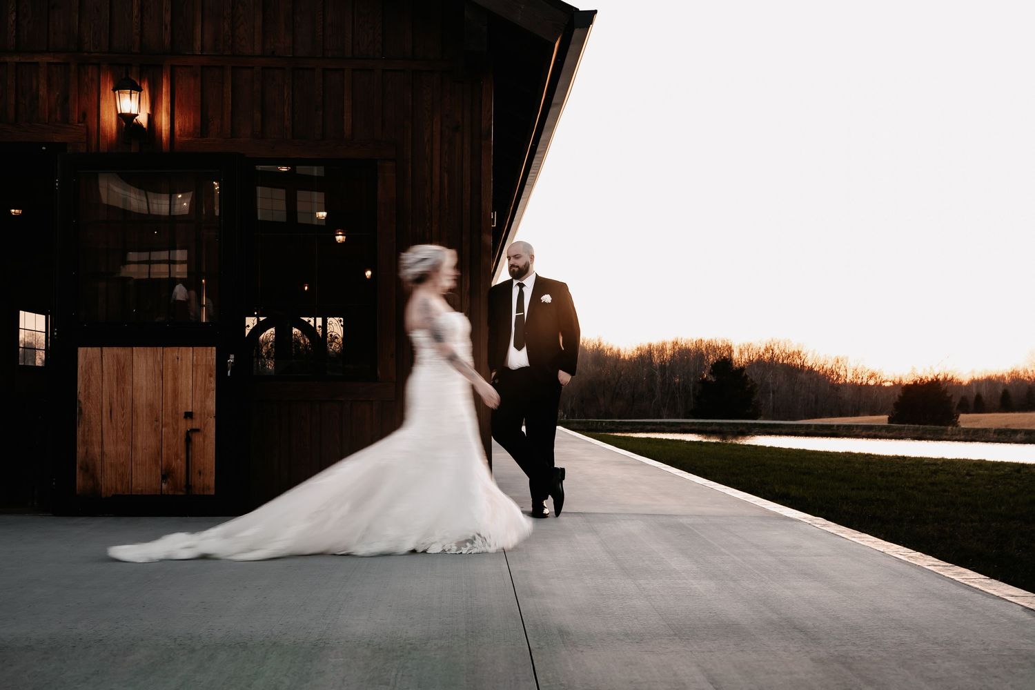 Bride and groom walking outside rustic barn wedding venue at golden hour sunset.