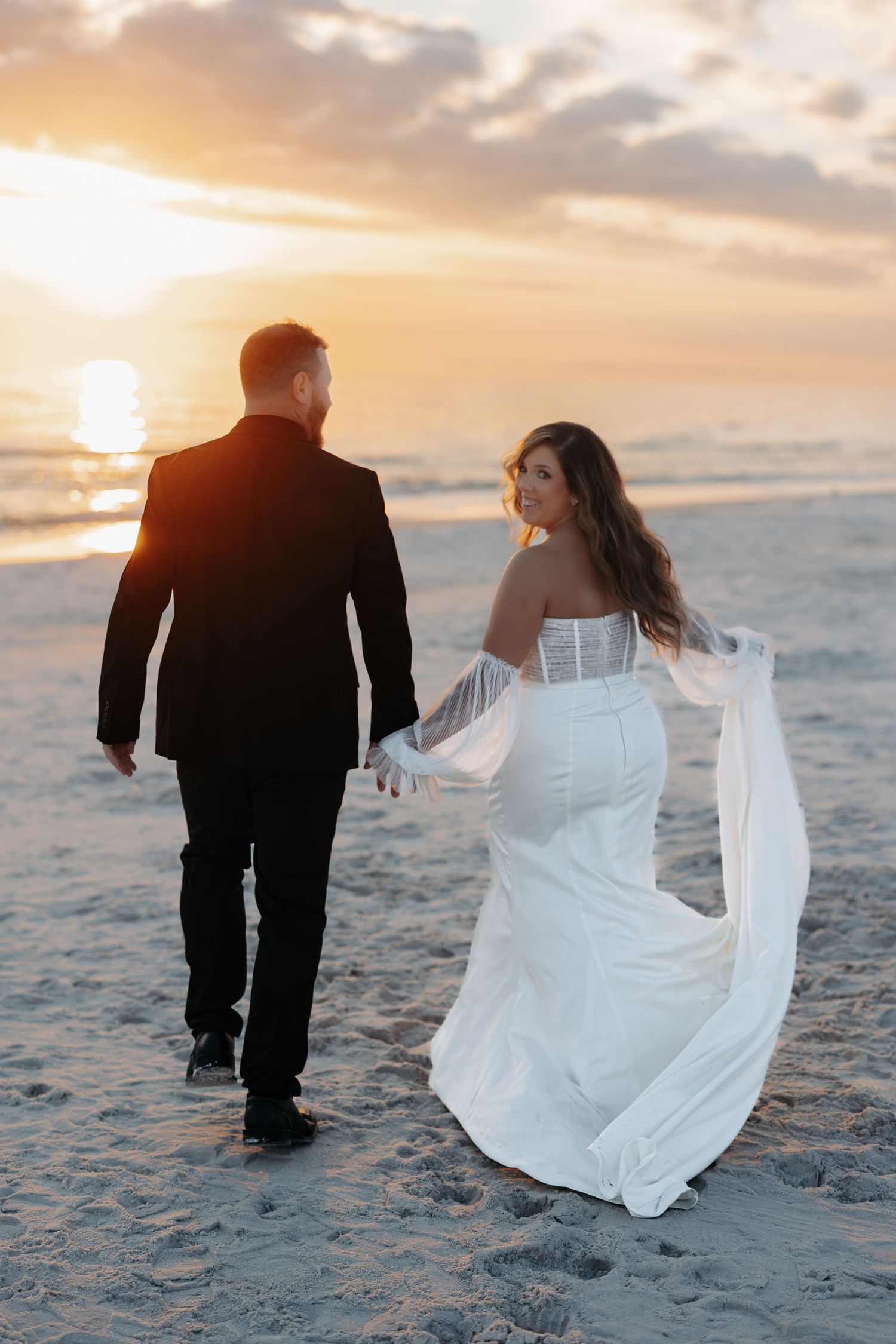 A couple in wedding attire walks along a sandy beach at sunset with their backs to the camera.
Powel Crosley Estate