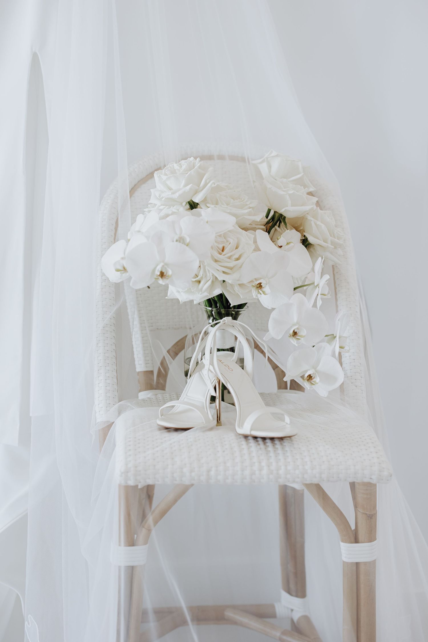 White orchid bouquets arranged in glass vases on wooden chairs create an elegant wedding ceremony aisle decoration.