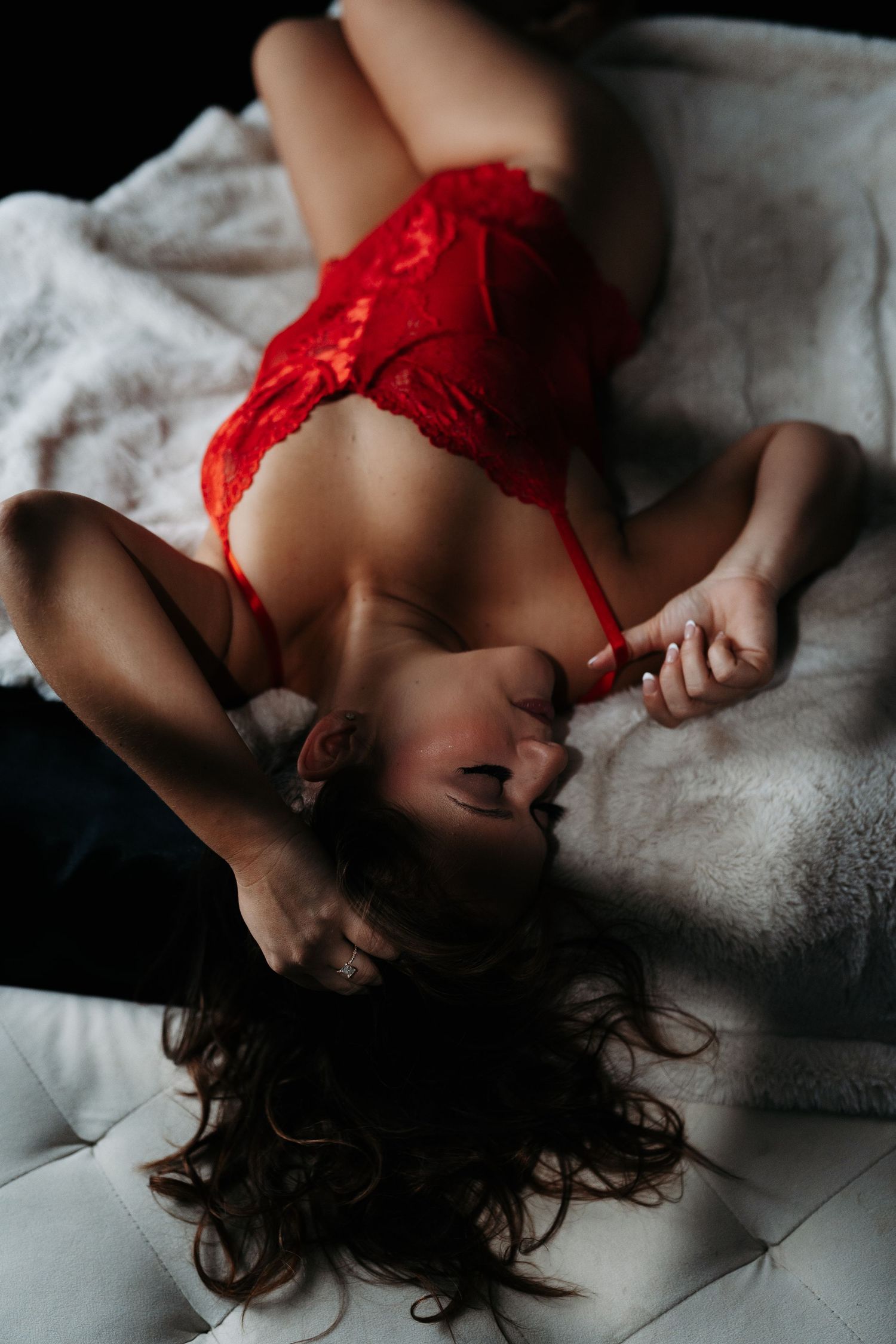 Woman in red lace lingerie lying on a white tufted surface in a boudoir photography pose.